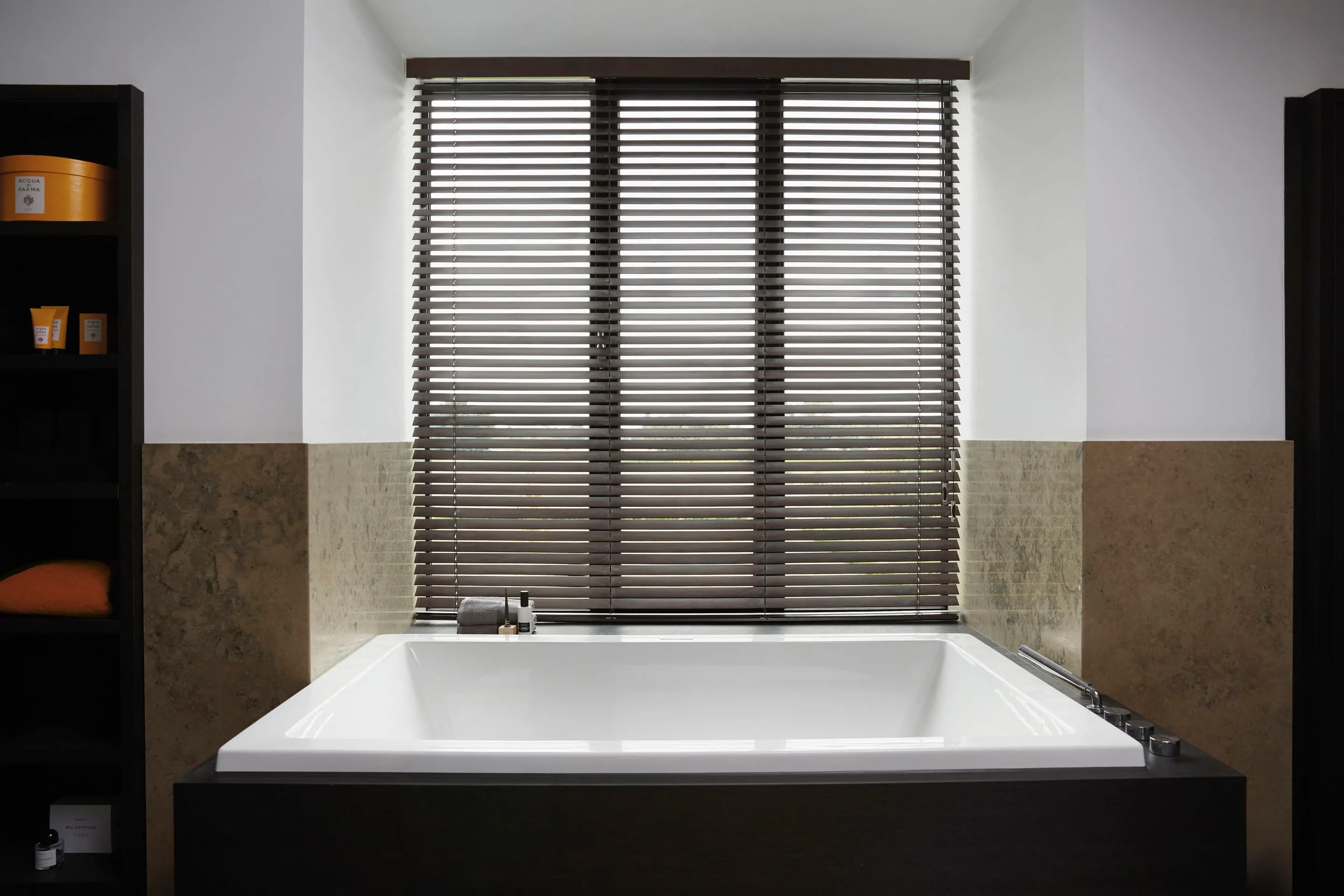 Brown wooden blinds in a bathroom behind a large, white bath tub
