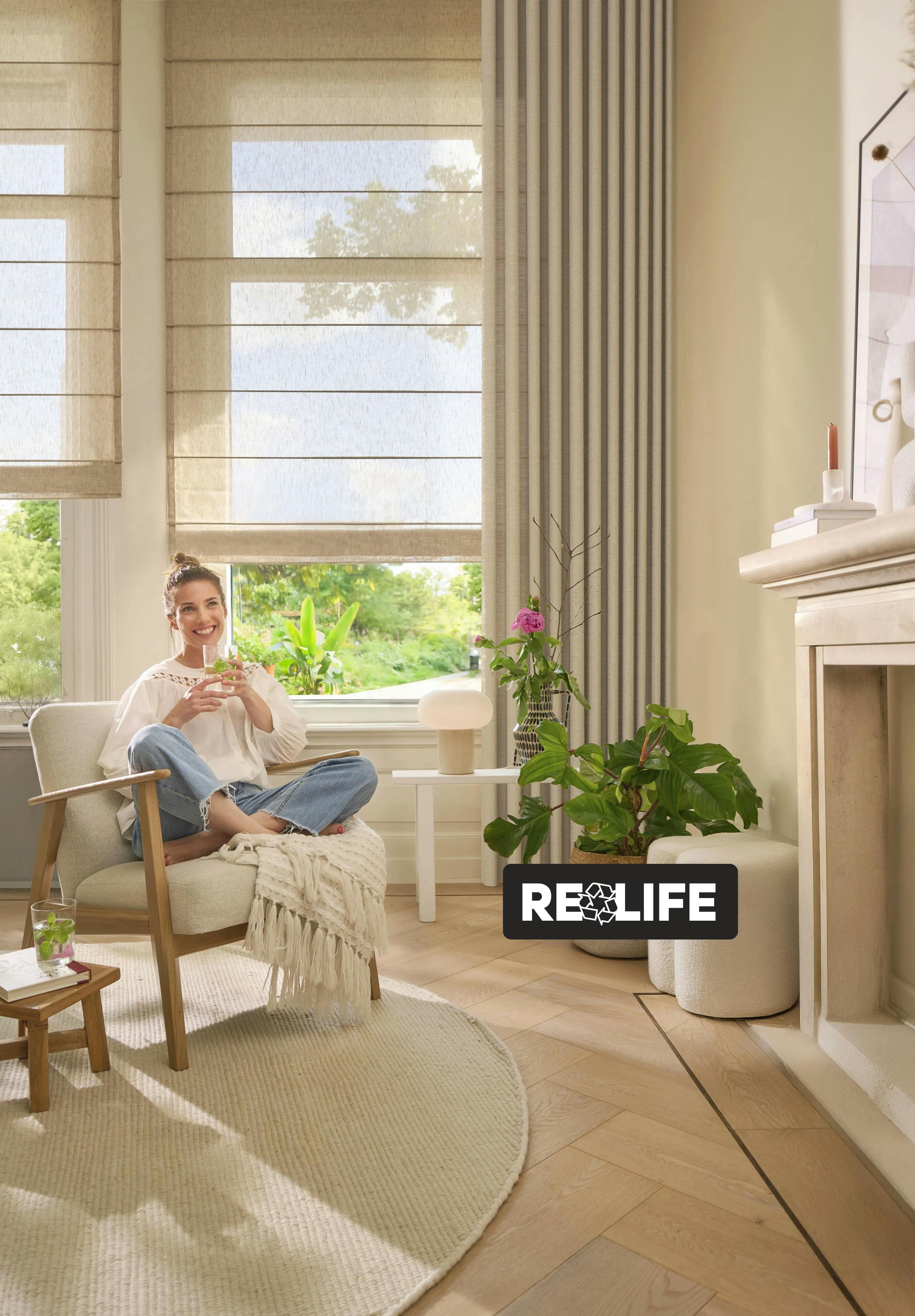 Een vrouw in een fauteuil in een knusse woonkamer met crèmekleurige vouwgordijnen en gordijnen voor de ramen