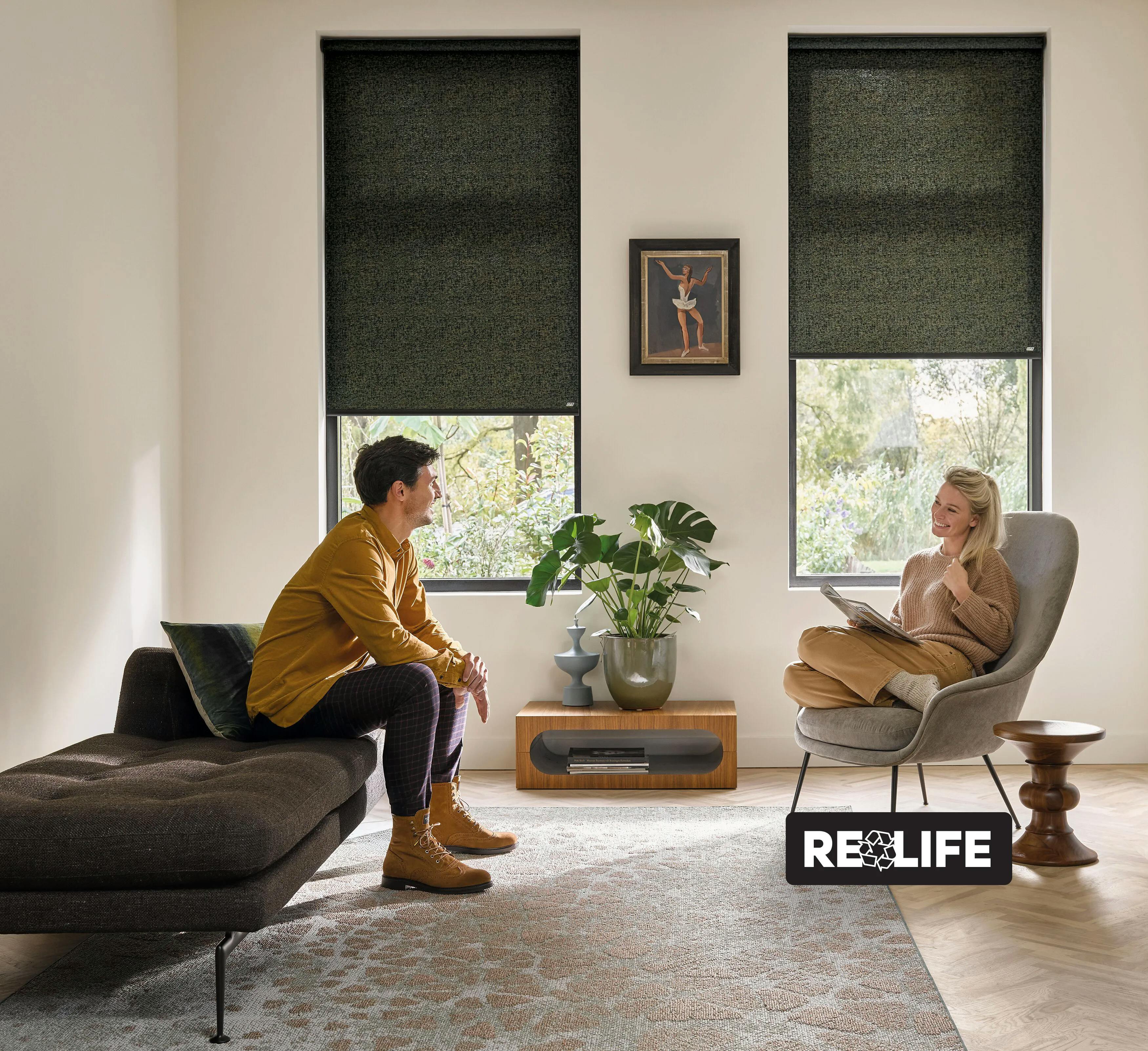A man and a woman sitting in a modern living room with green roller blinds on windows