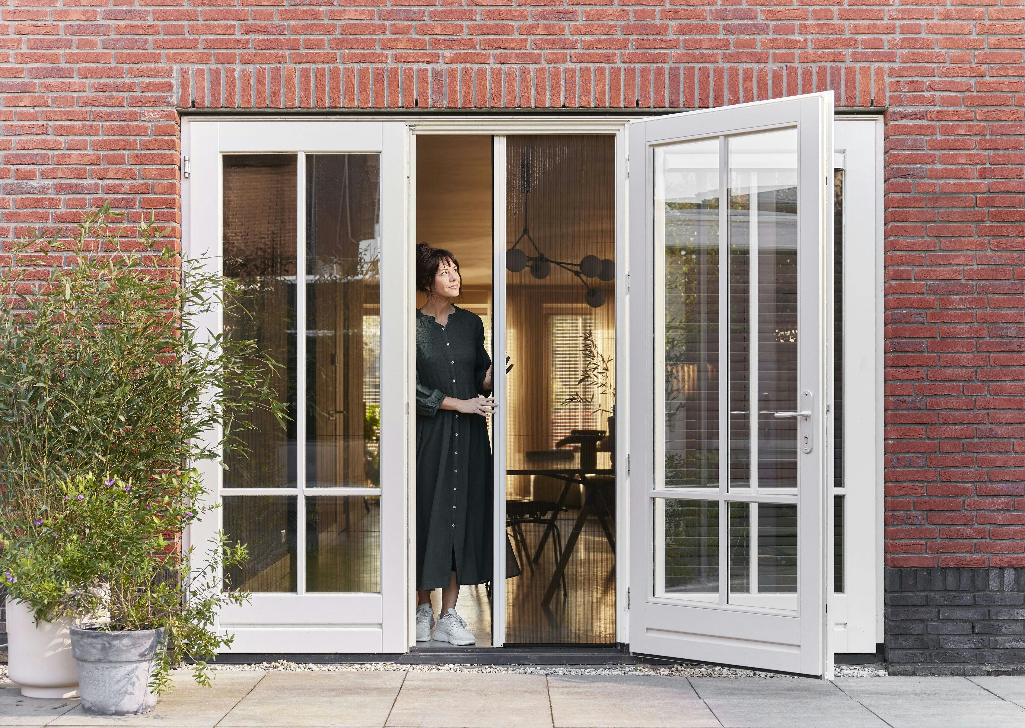 En kvinde åbner en plissédør med insektnet på franske døre