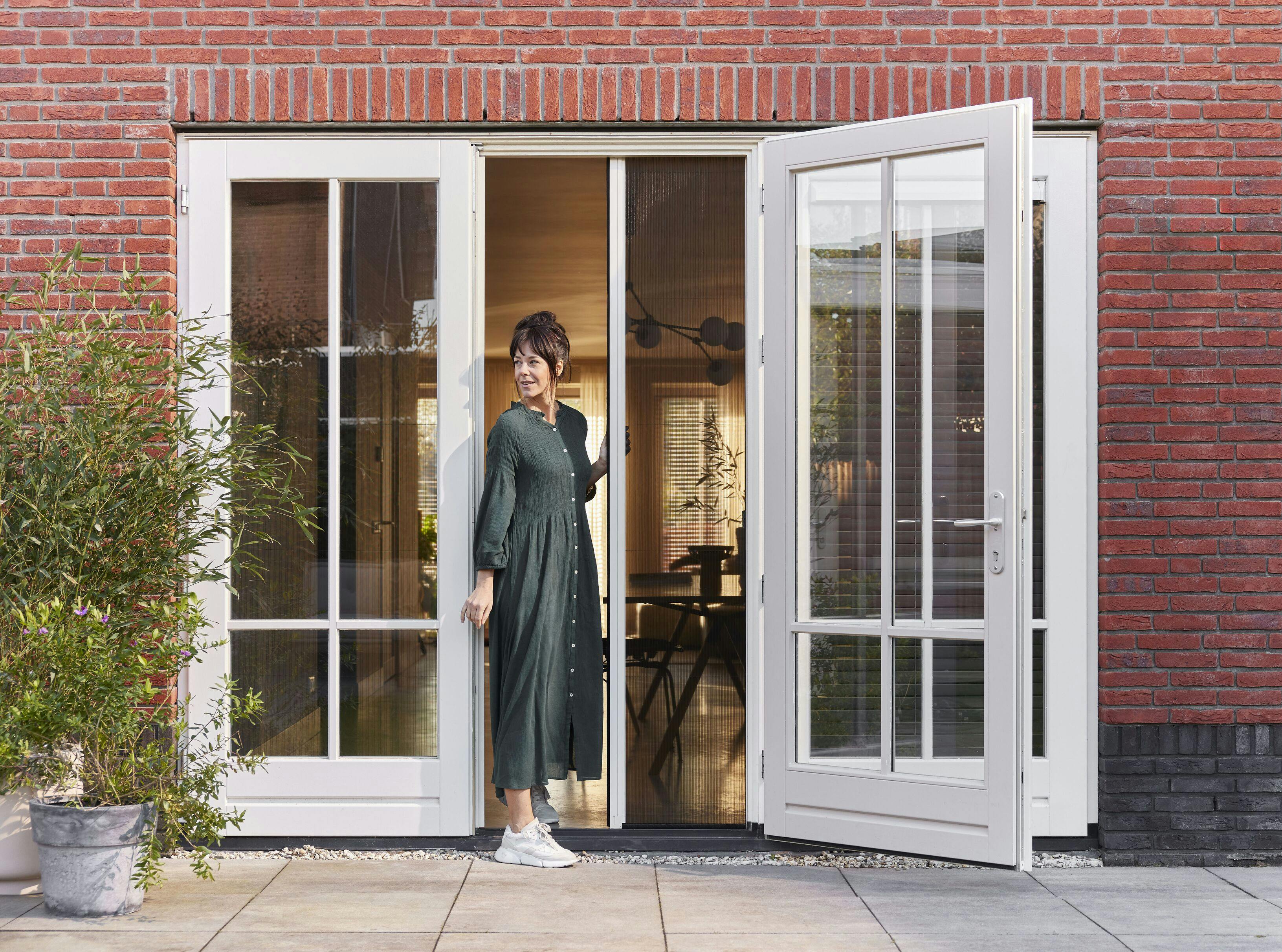 Een vrouw die een plissé hordeur opent bij openslaande deuren