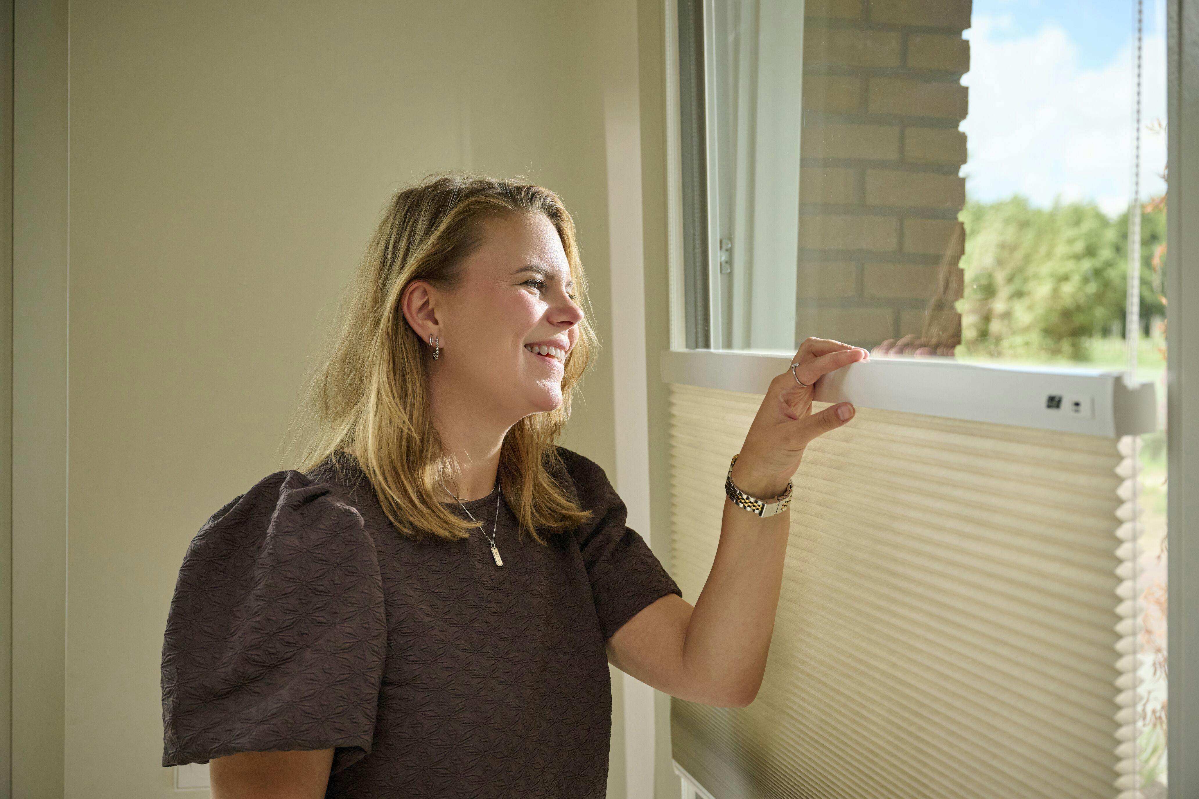 A woman looking through a window with cream top down / bottom up duette shades