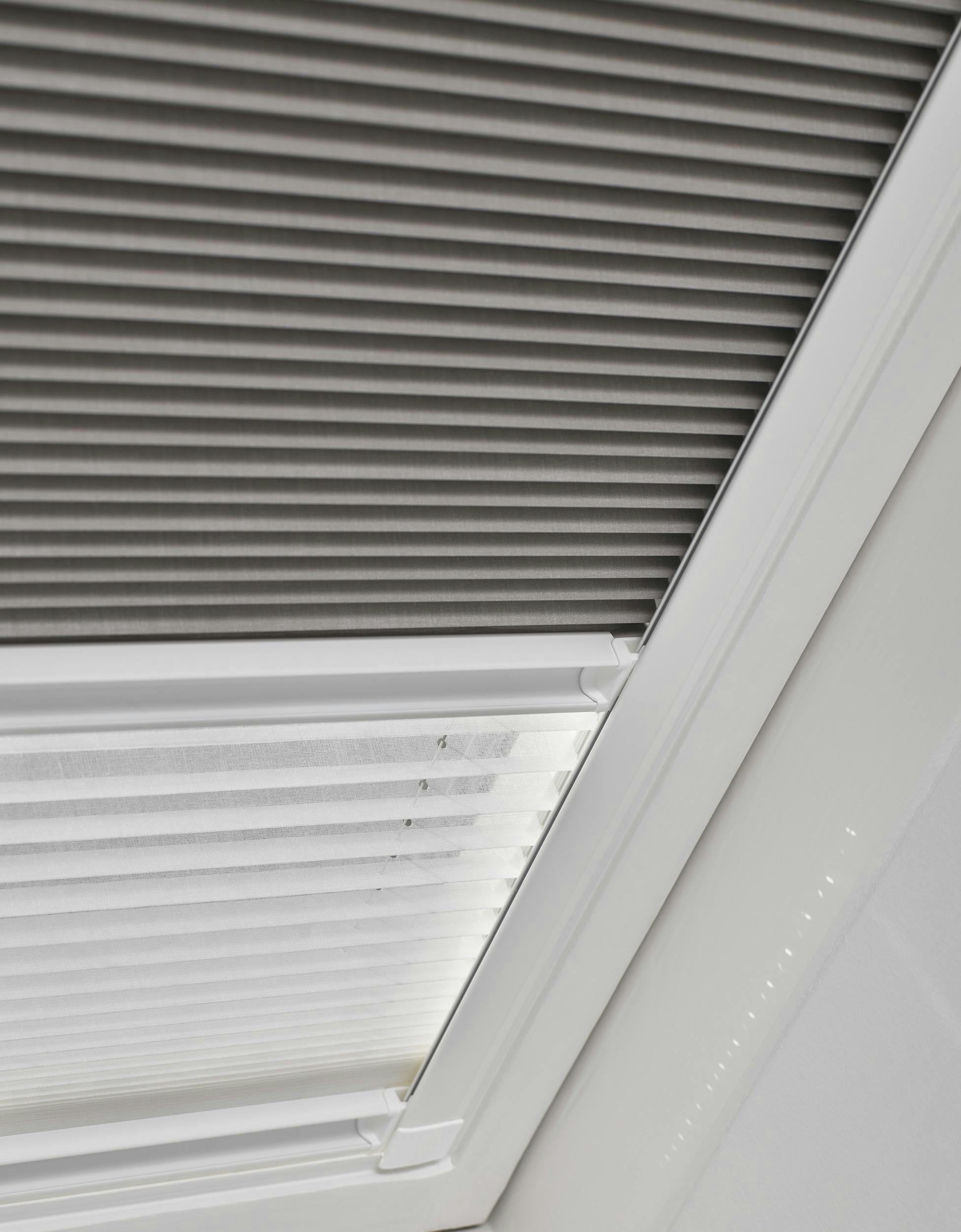 Gros plan sur des stores Duette® jour nuit gris sur une fenêtre de toit