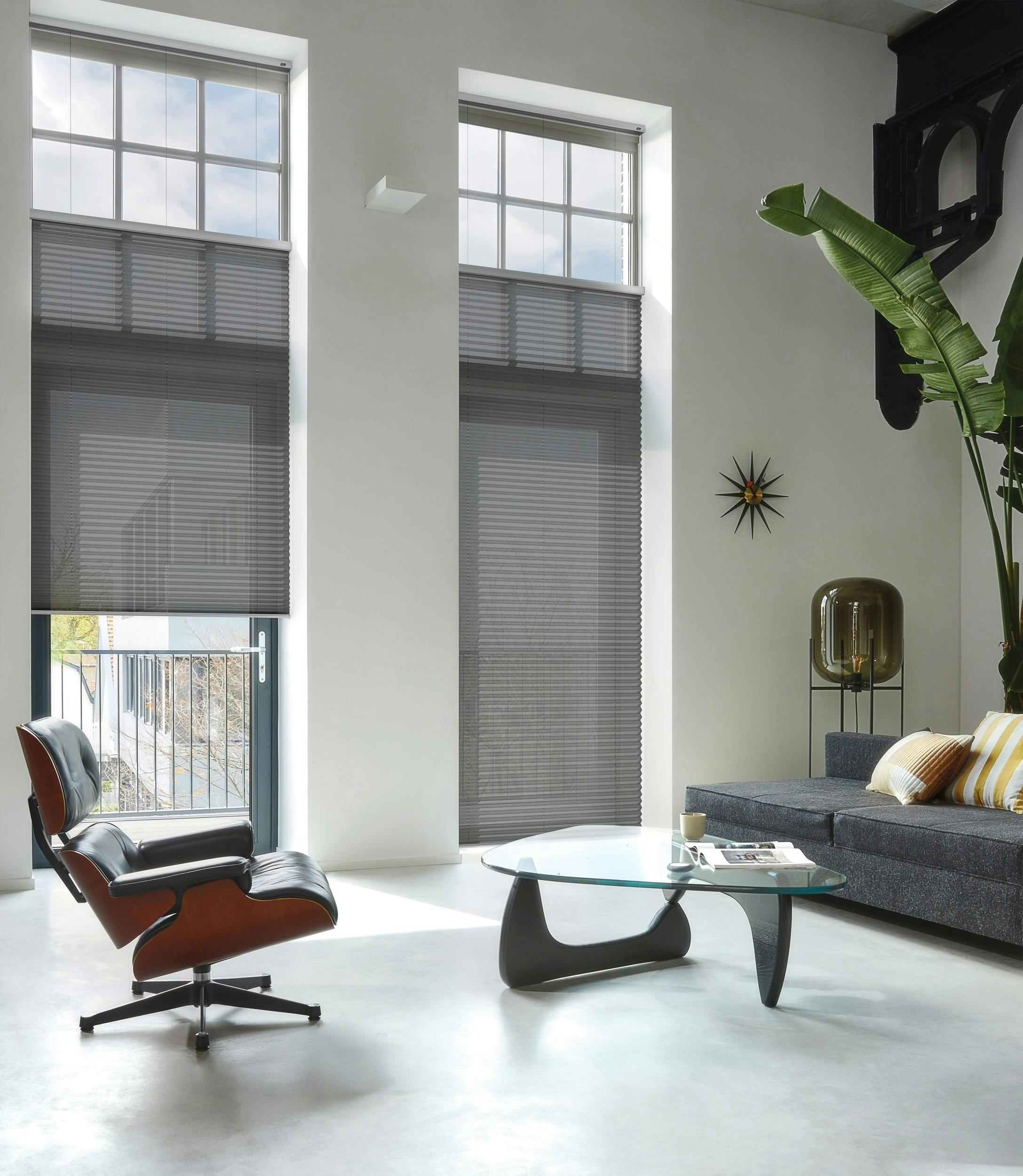 Donkergrijze plissé shades op een grote deur en raam in een moderne woonkamer