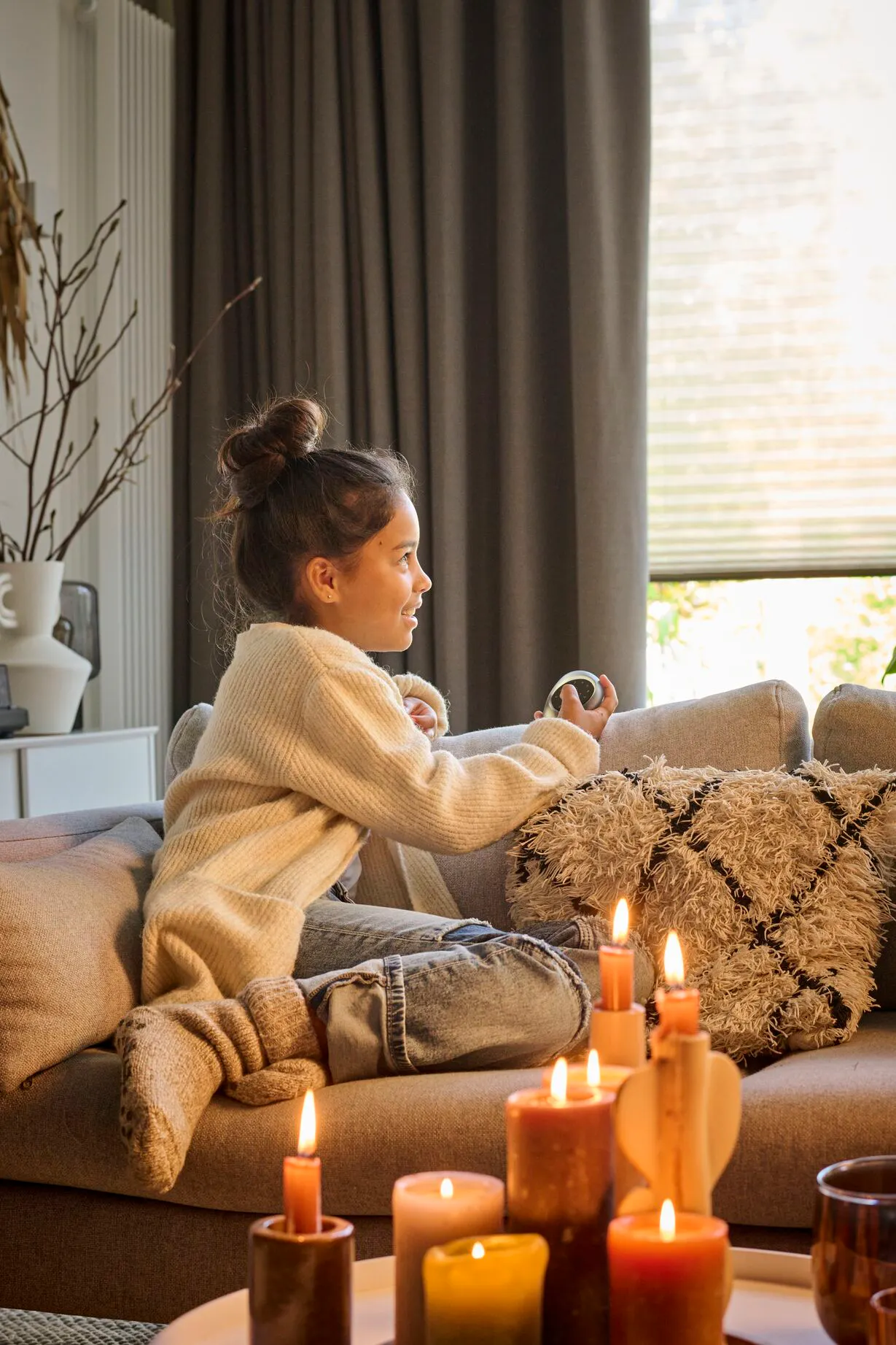 A girl drinking in a cozy living room with white duette blinds layered with brown curtains