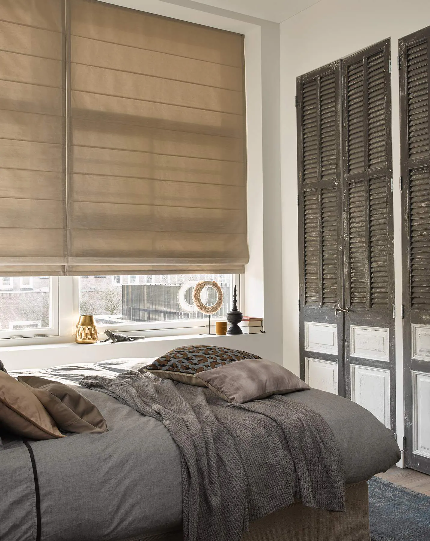 Beige roman blinds and brown shutters in a bedroom