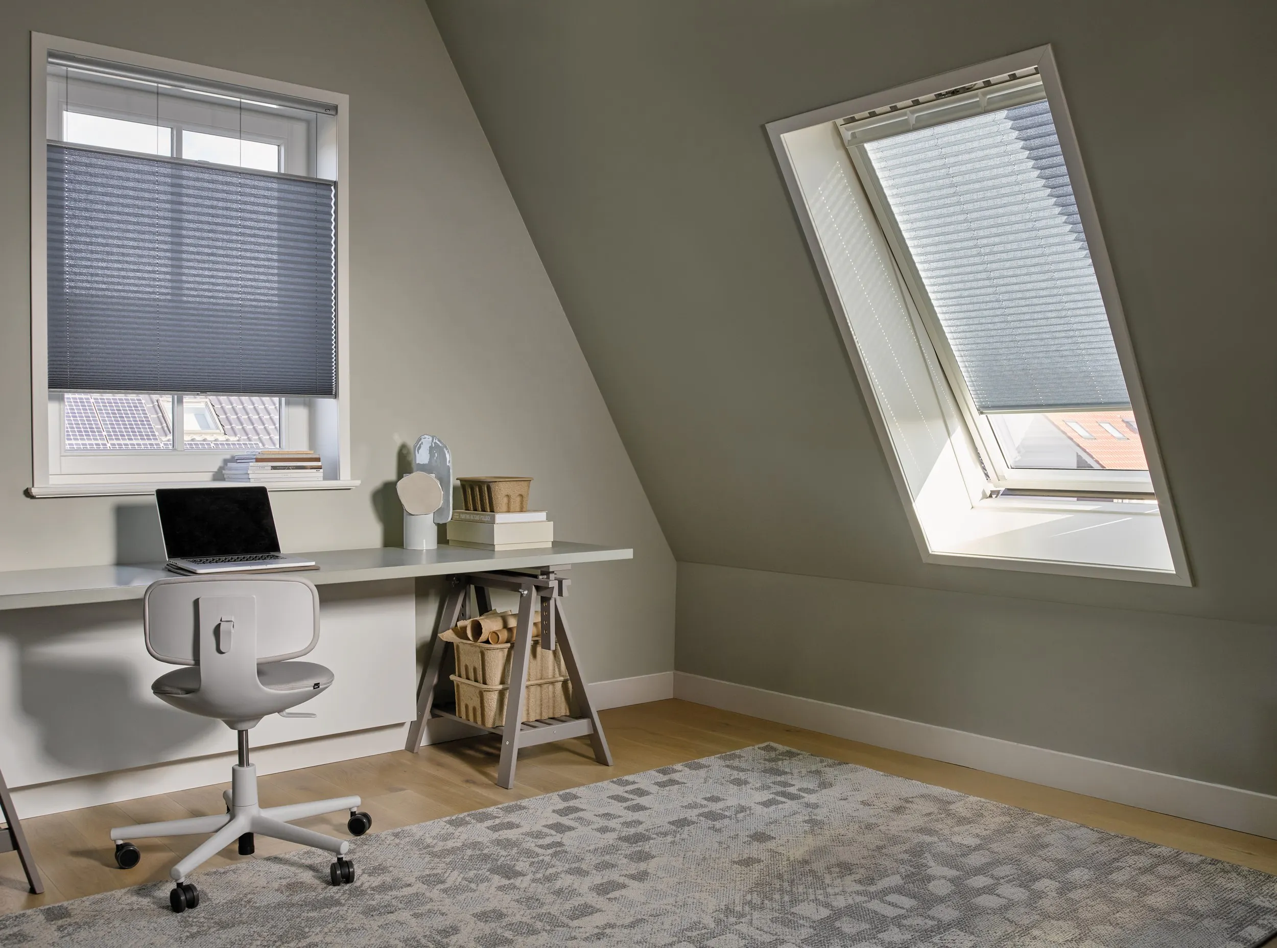 Blauwe plissé gordijnen op een standaard raam en dakraam in een thuiskantoor op zolder