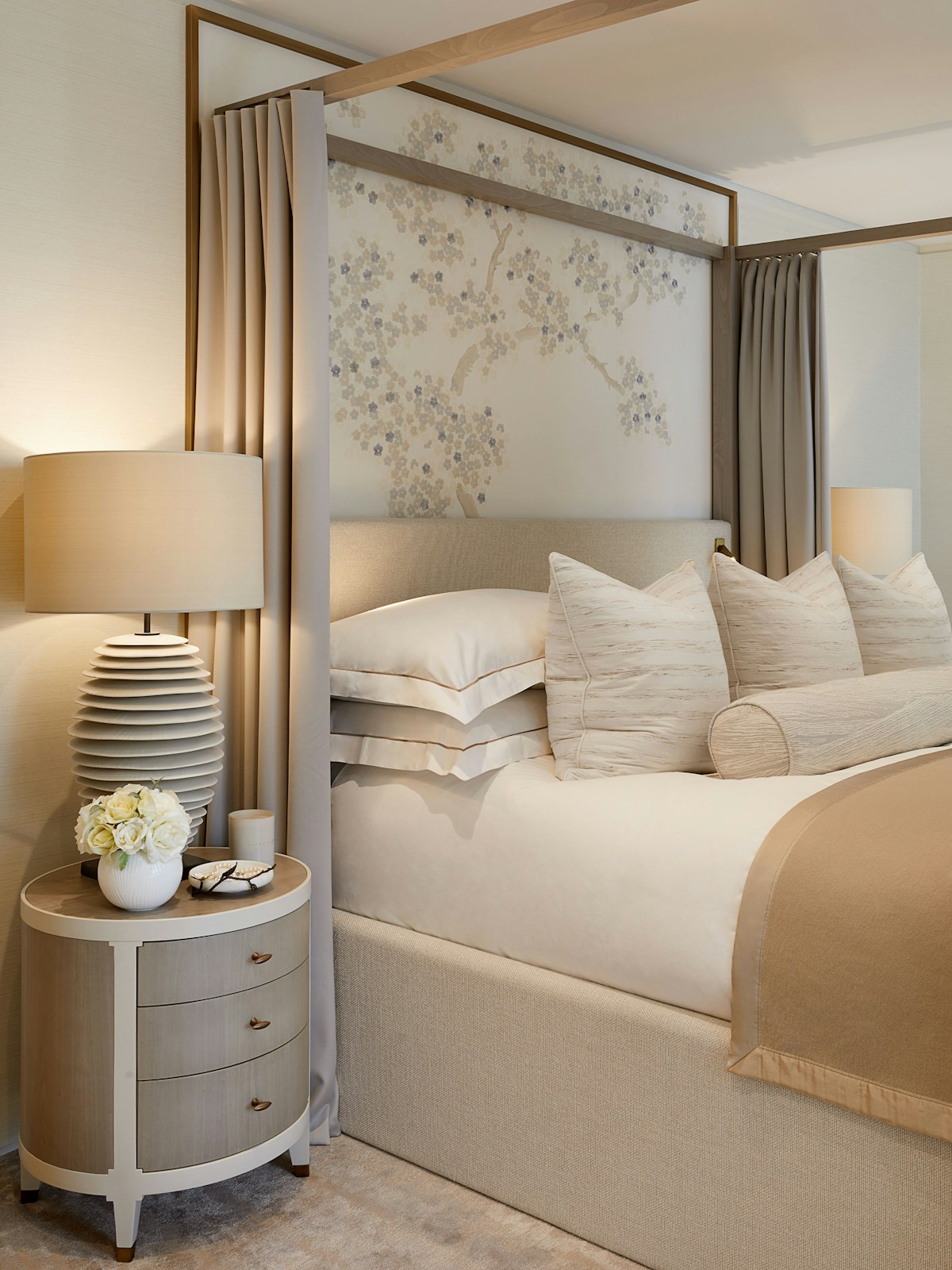 Neutral toned bedroom with curved bedside table and four-poster bed with beige throw