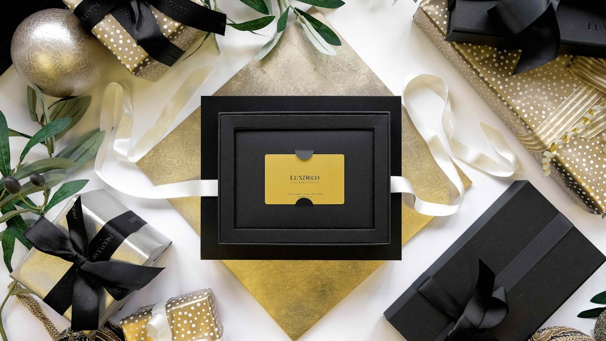 Golden LuxDeco gift card in presentation box next to beautifully wrapped Christmas gifts