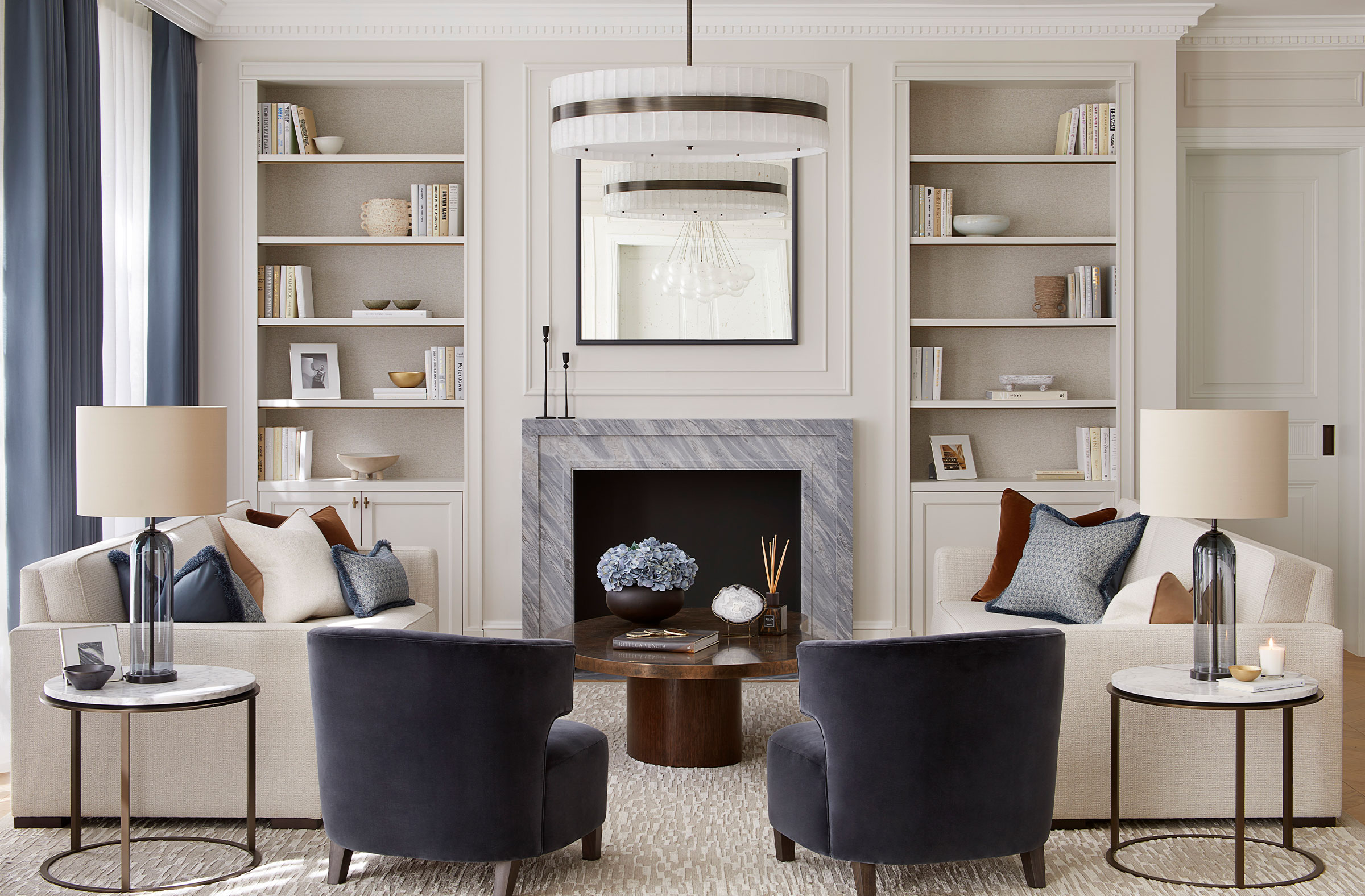 Classic contemporary living room by designer Andrea Benedettini in blue and white, two blue velvet armchairs, marble side tables and white sofas
