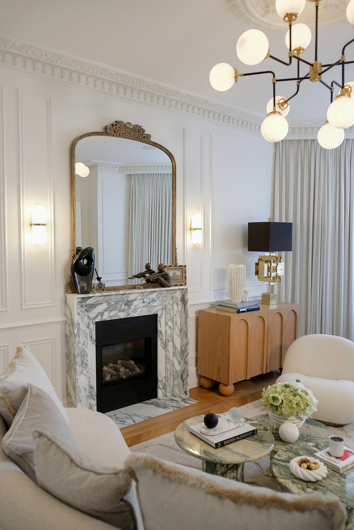 Camila Carril marble mantle piece with large gilt mirror, modern chandelier and cream boucle armchair