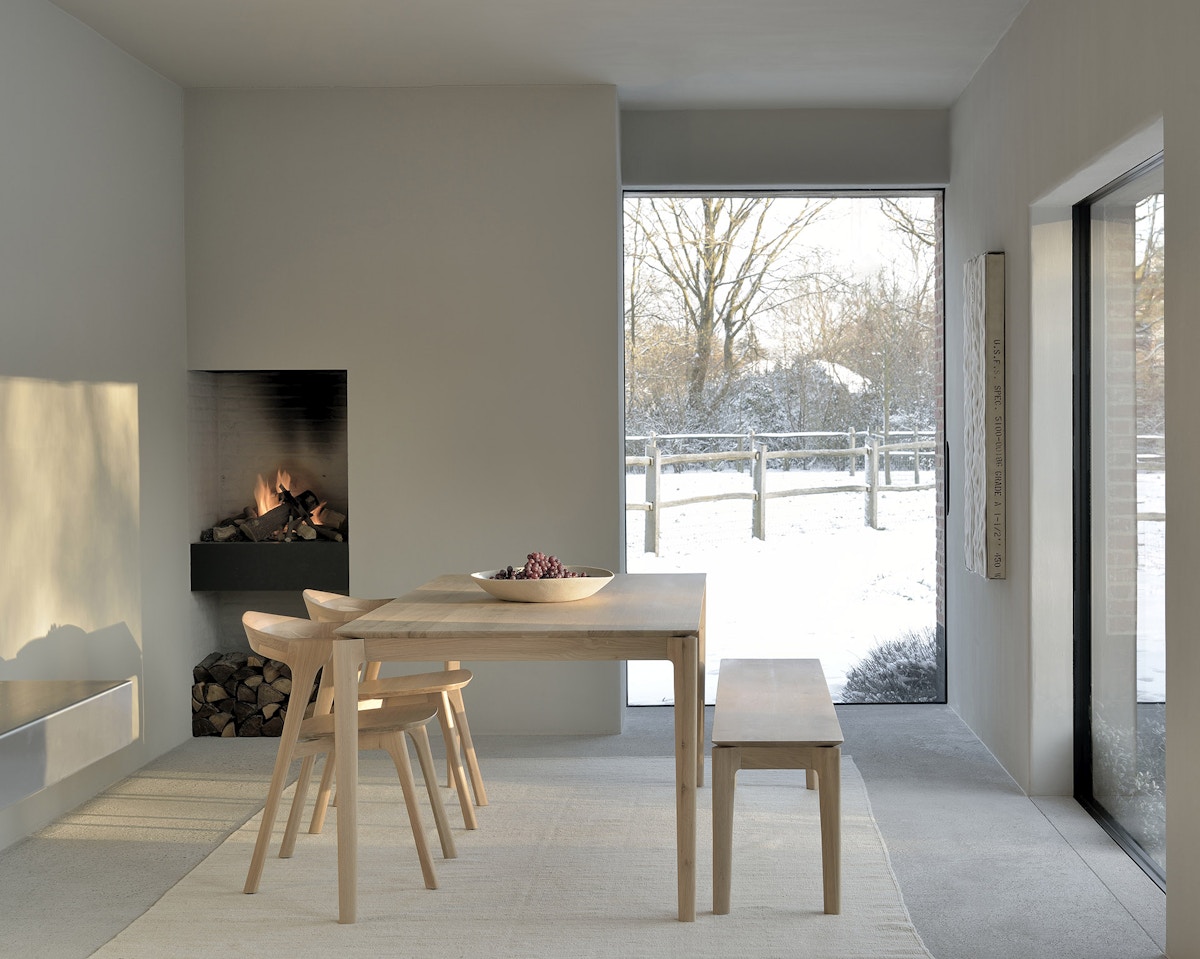 Ethnicraft Bok oak dining chair and table beside open fire against a snowy backdrop