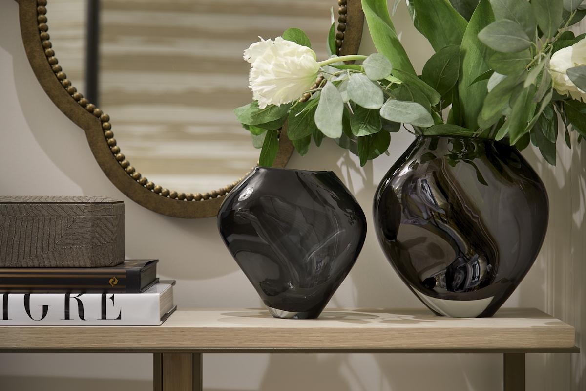 Console table vignette with two glass grey vases—one with white tulips in it—a textured bronze jewellery box and a quatrefoil mirror