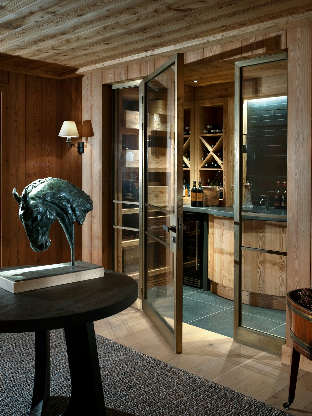 Nicky Dobree winter chalet with bronze horse statue on black wooden table, glass door opening into a wine cellar.