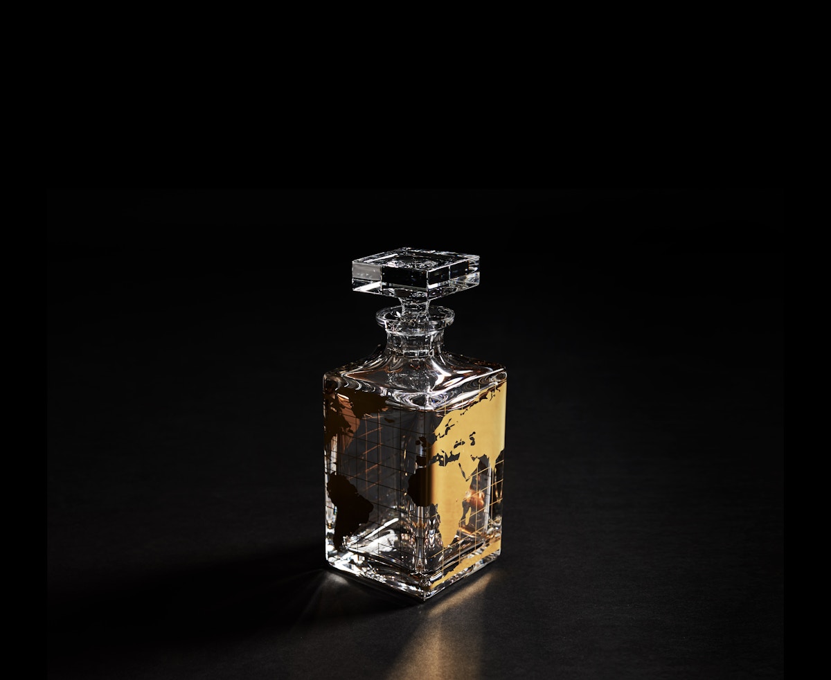 A crystal whisky decanter featuring a map of the world in gold against a black background