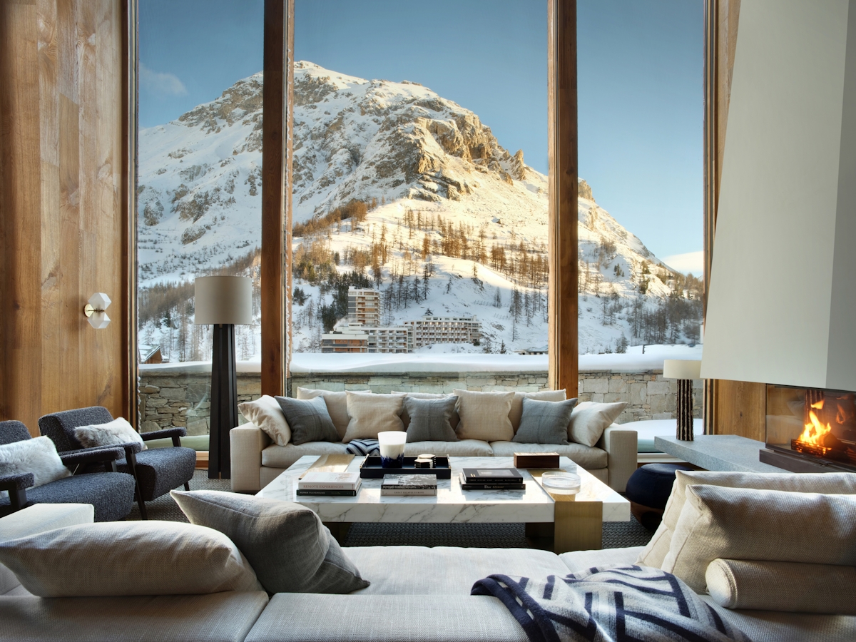 Nicky Dobree designed chalet featuring open fireplace, large seating area around marble coffee table and view of large snowy mountain