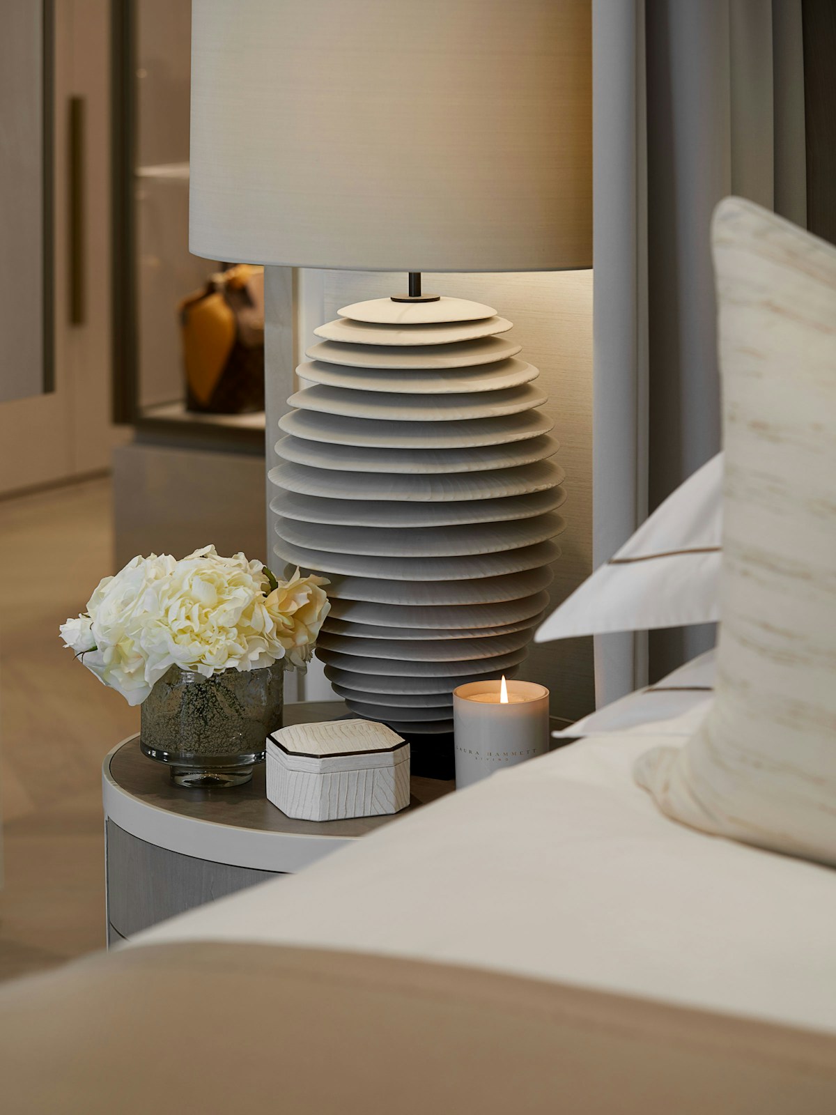 Ceramic table lamp in grey-white on bedsode table, with small peony blossom vase and trinket box and candle