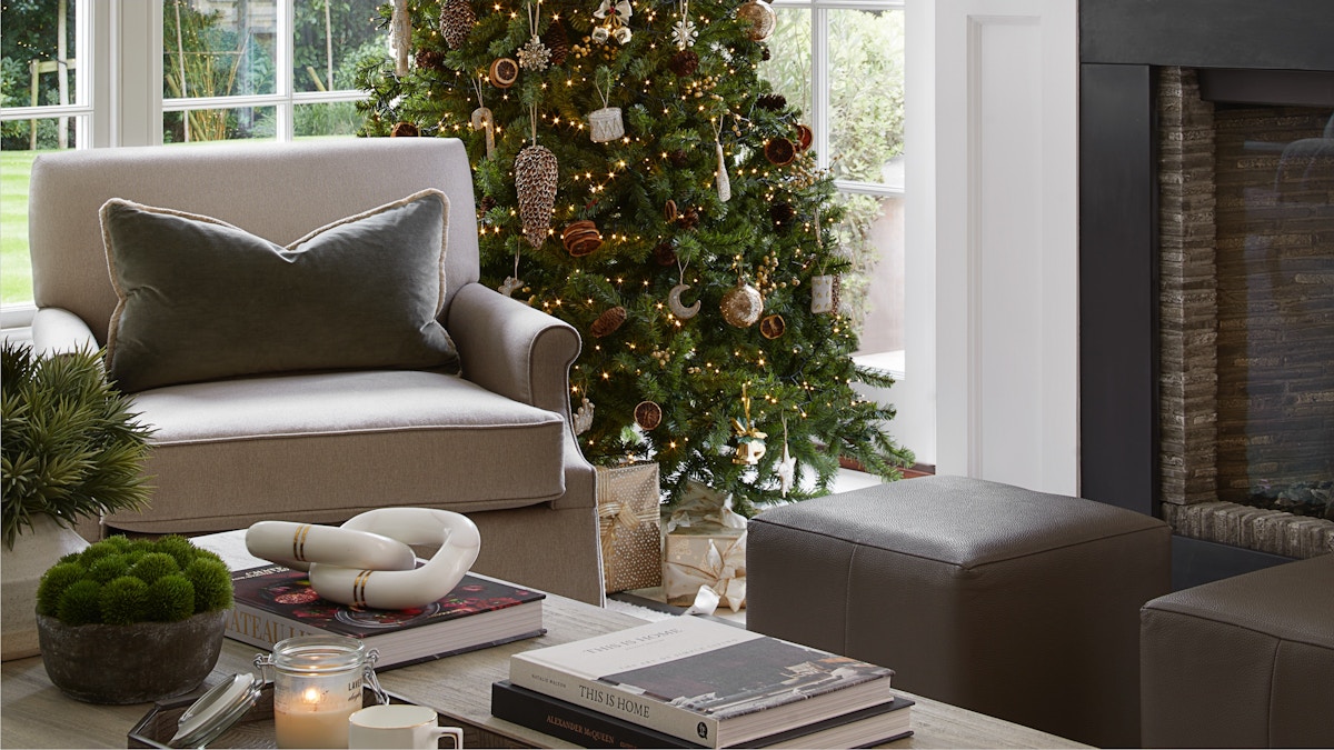 A festive living room featuring a Christmas tree full of designer Christmas decorations, an open fireplace, luxury furniture and beautiful home accessories