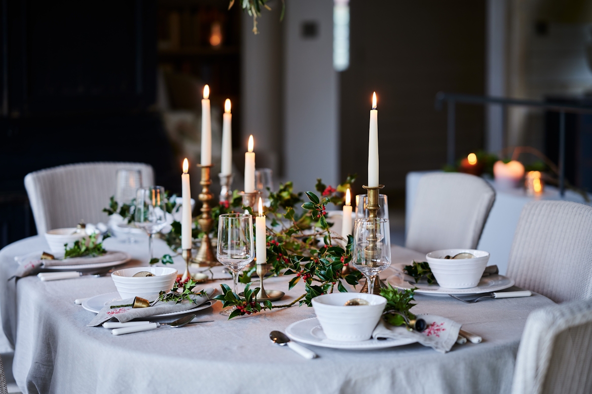 Christmas dining table with white tablecloth and holly branches 