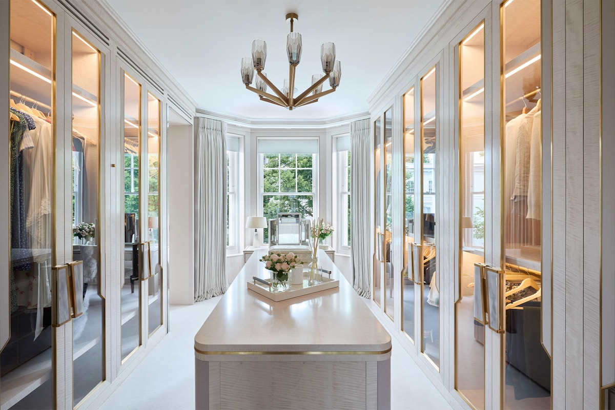 Large, bright dressing room with chandelier and island cabinet unit with tray on top
