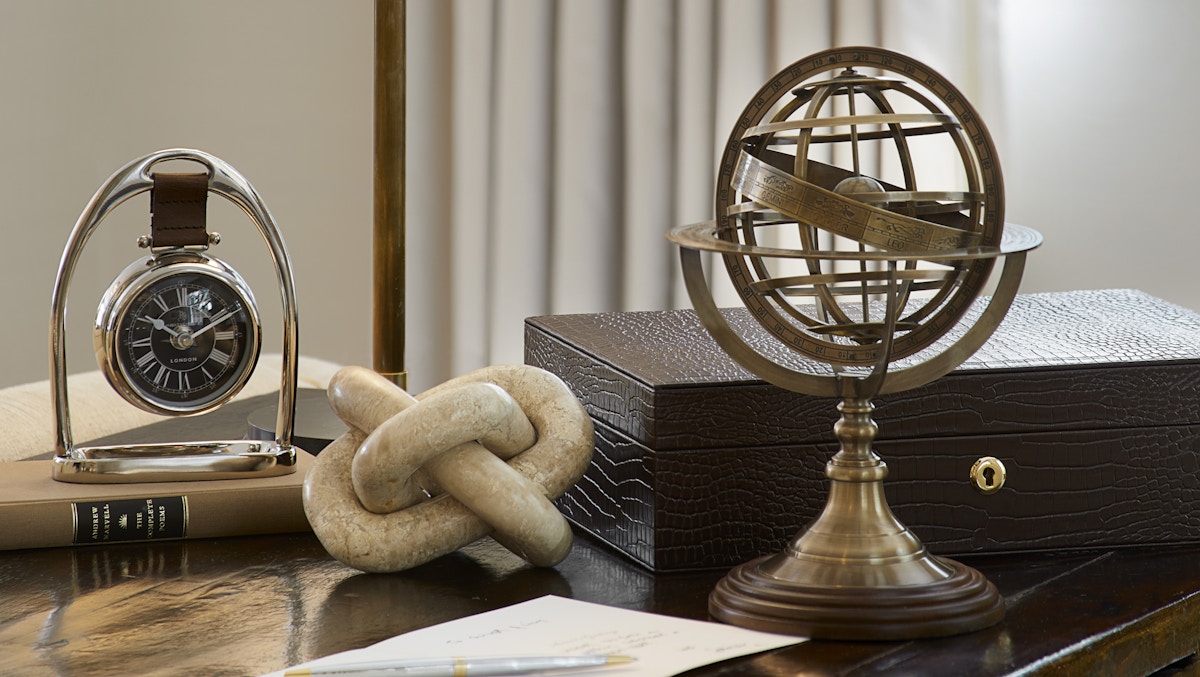 A desktop with desk accessories, brass globe ornament, clock, leather box