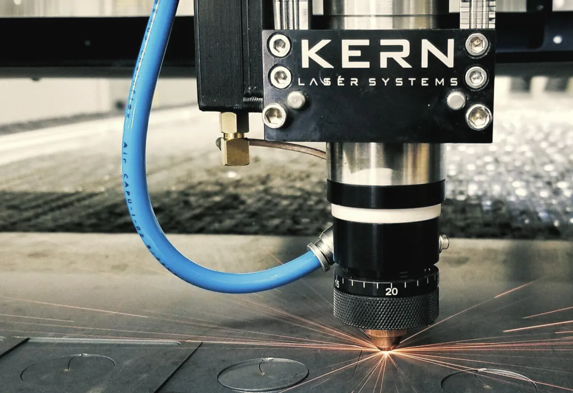 Kern Laser Systems laser cutting head cutting circular shapes from a sheet of metal, sparks flying from the cut point