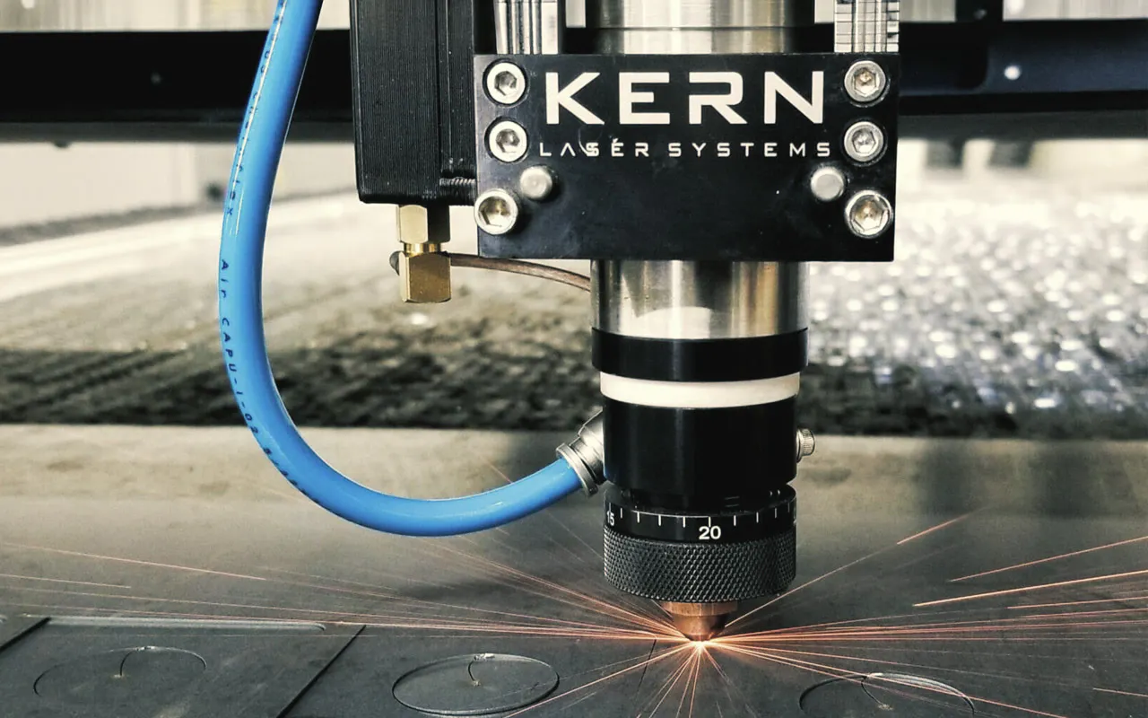 Kern Laser Systems laser cutting head cutting circular shapes from a sheet of metal, sparks flying from the cut point