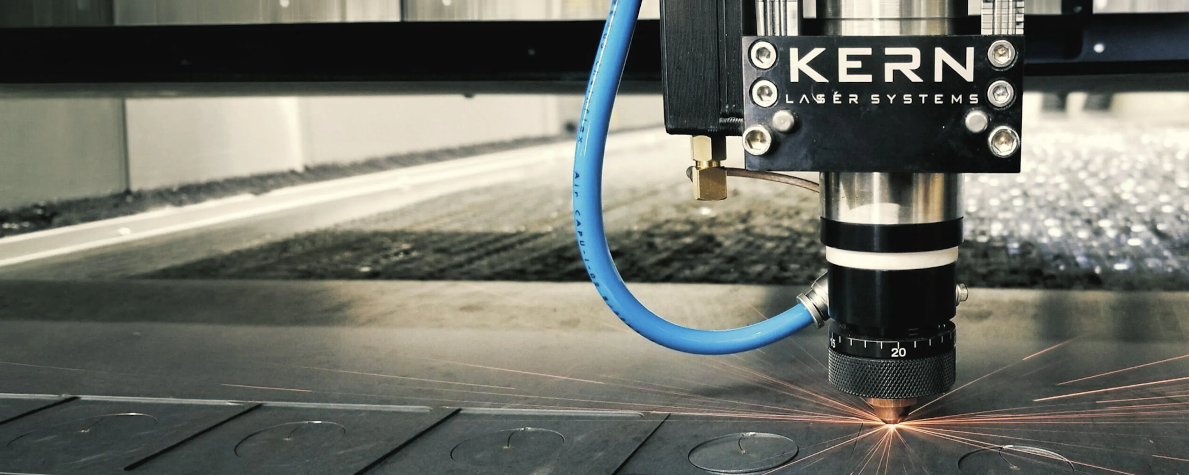 Kern Laser Systems laser cutting head cutting circular shapes from a sheet of metal, sparks flying from the cut point