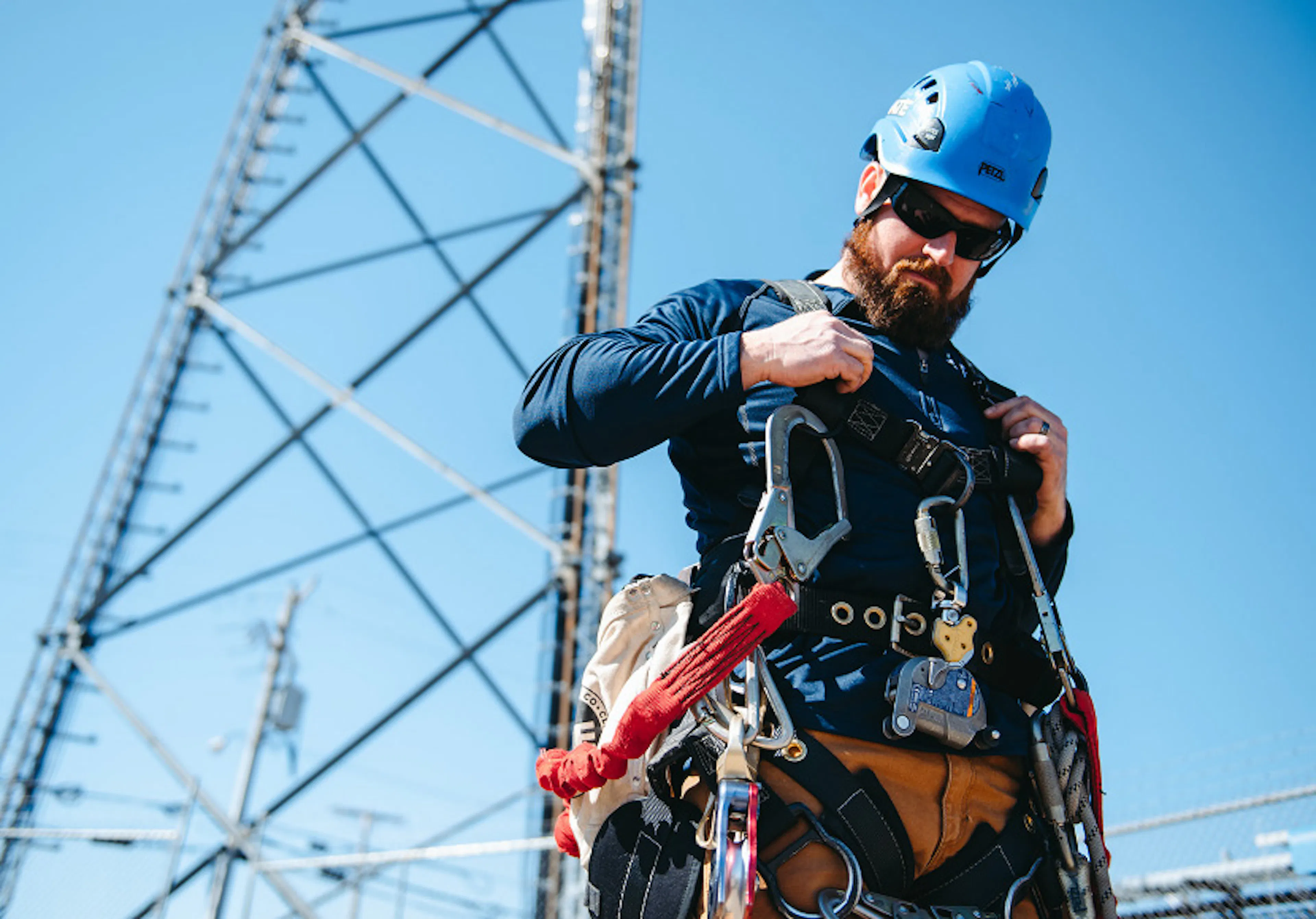 Technician in a helmet and safety harness gearing up at the base of a cell tower