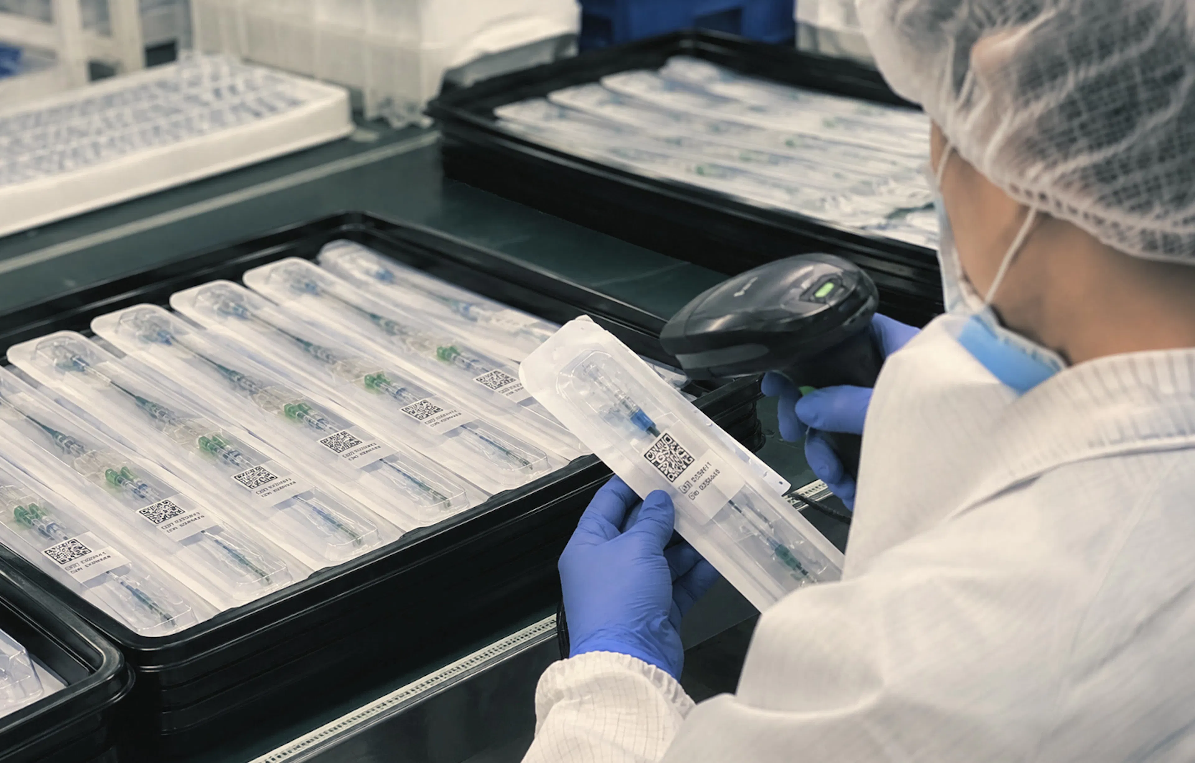 Technician in a hairnet and gloves scanning packaged medical device trays