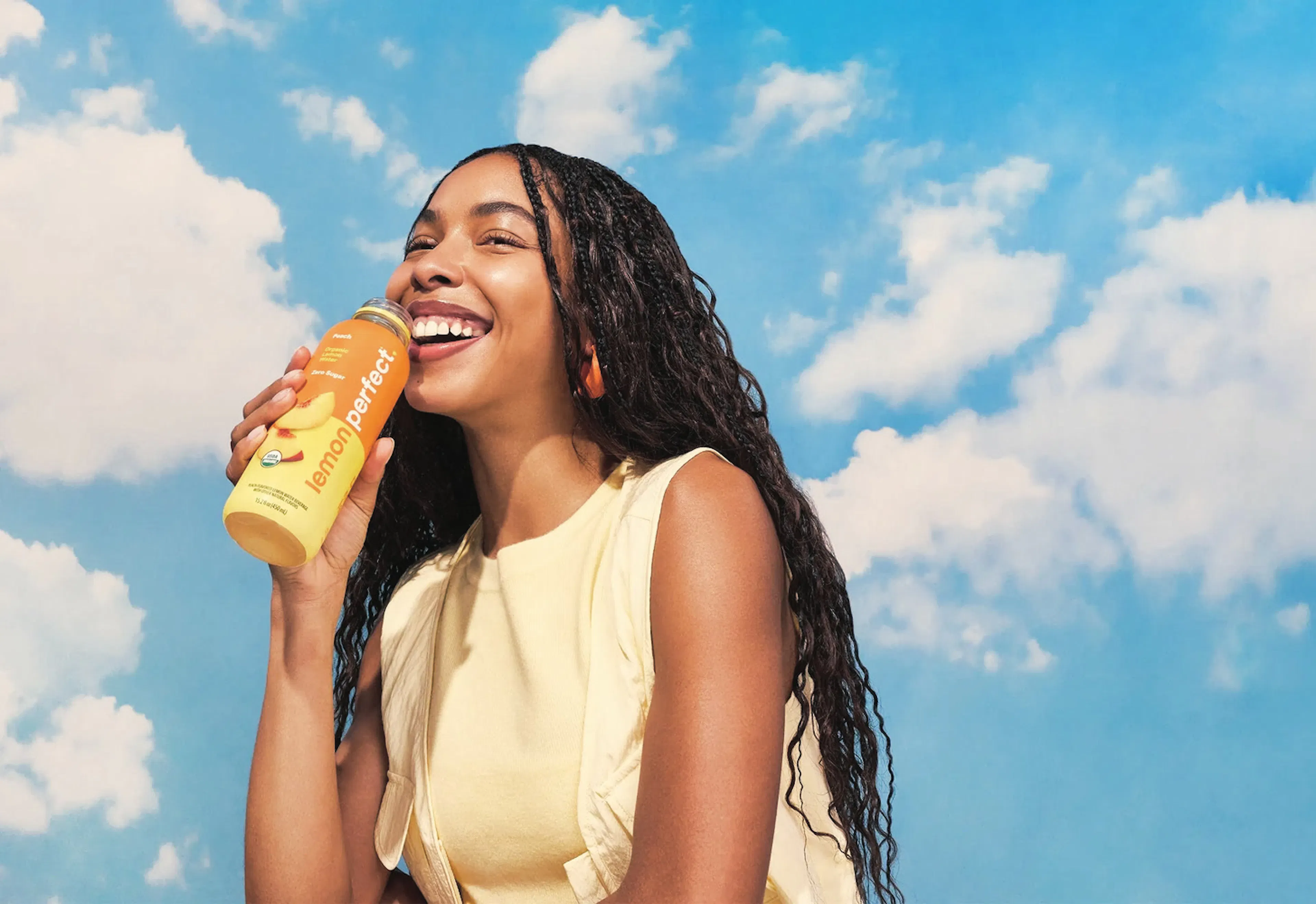Woman drinking a bottle of Lemon Perfect against a blue sky