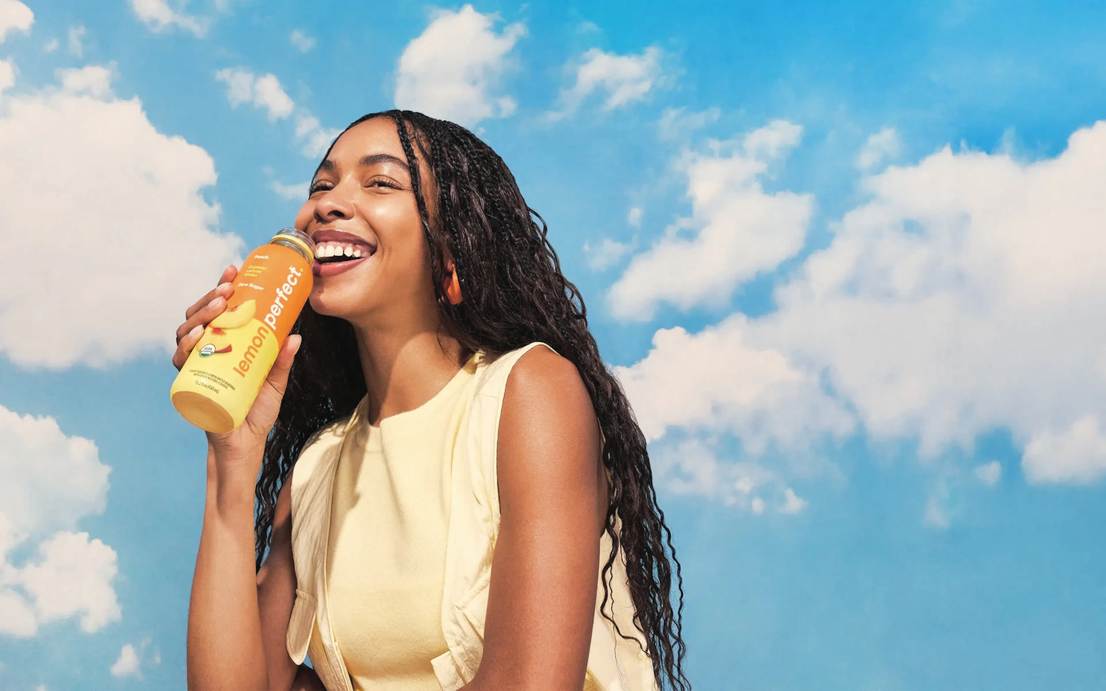 Woman drinking a bottle of Lemon Perfect against a blue sky