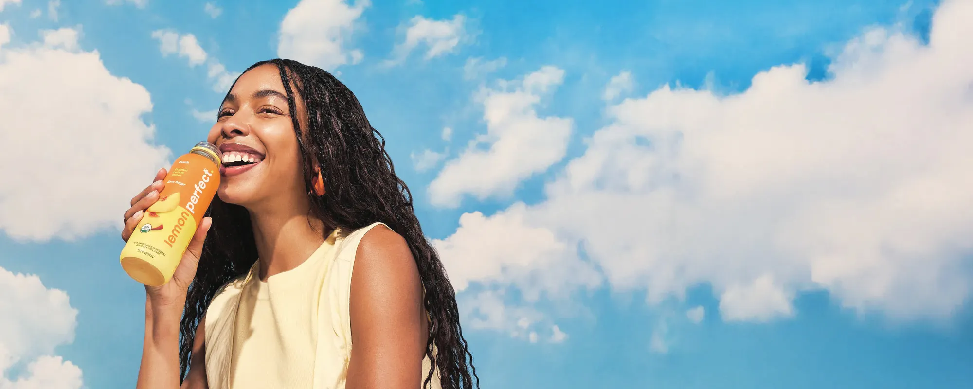 Woman drinking a bottle of Lemon Perfect against a blue sky
