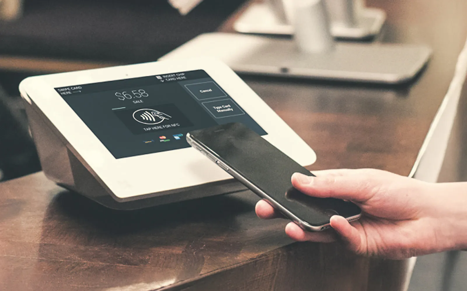 Customer tapping a phone to pay at a Brilliant POS tablet terminal