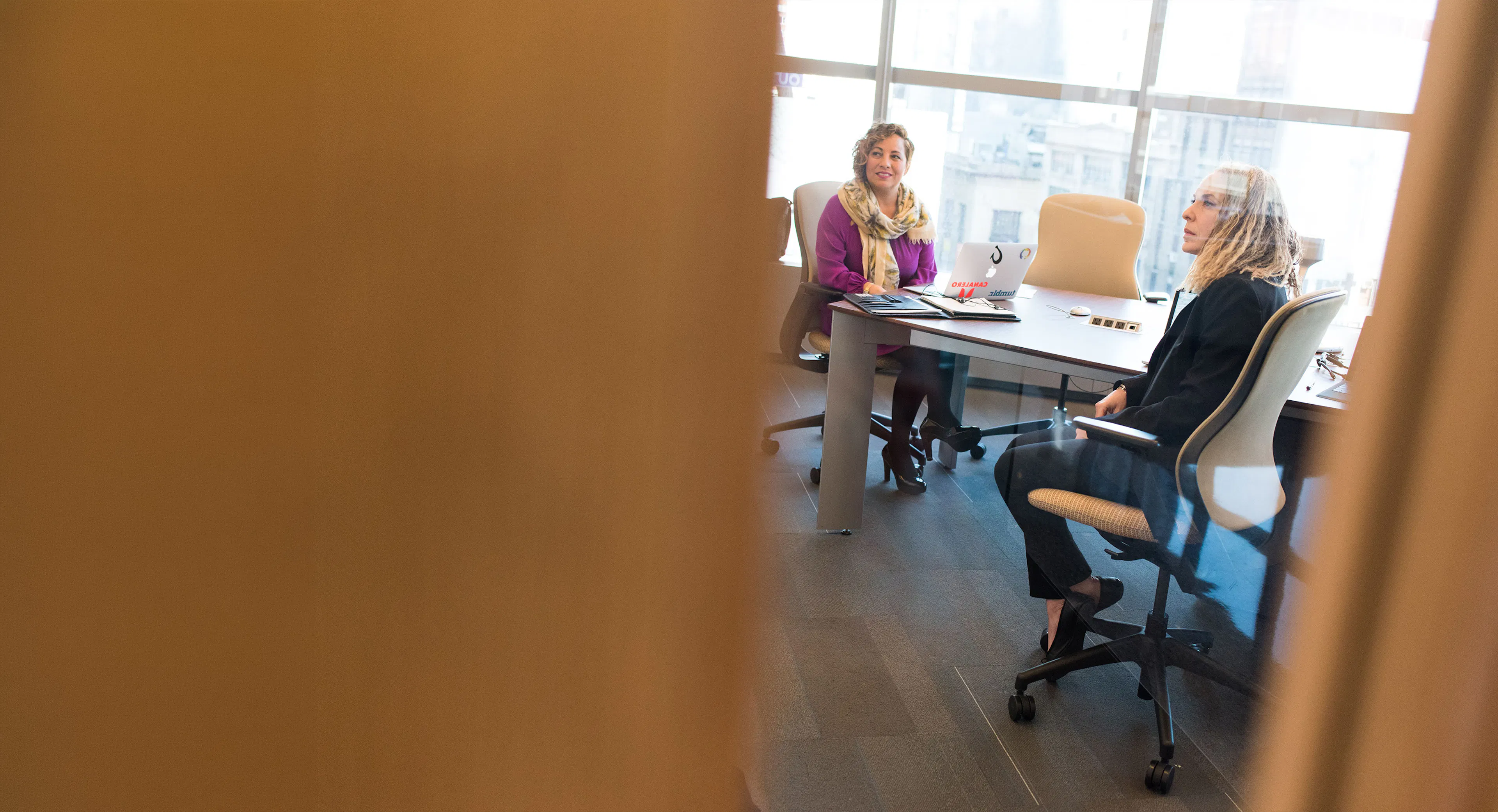 Two colleagues meeting at a table beside a window in a modern office