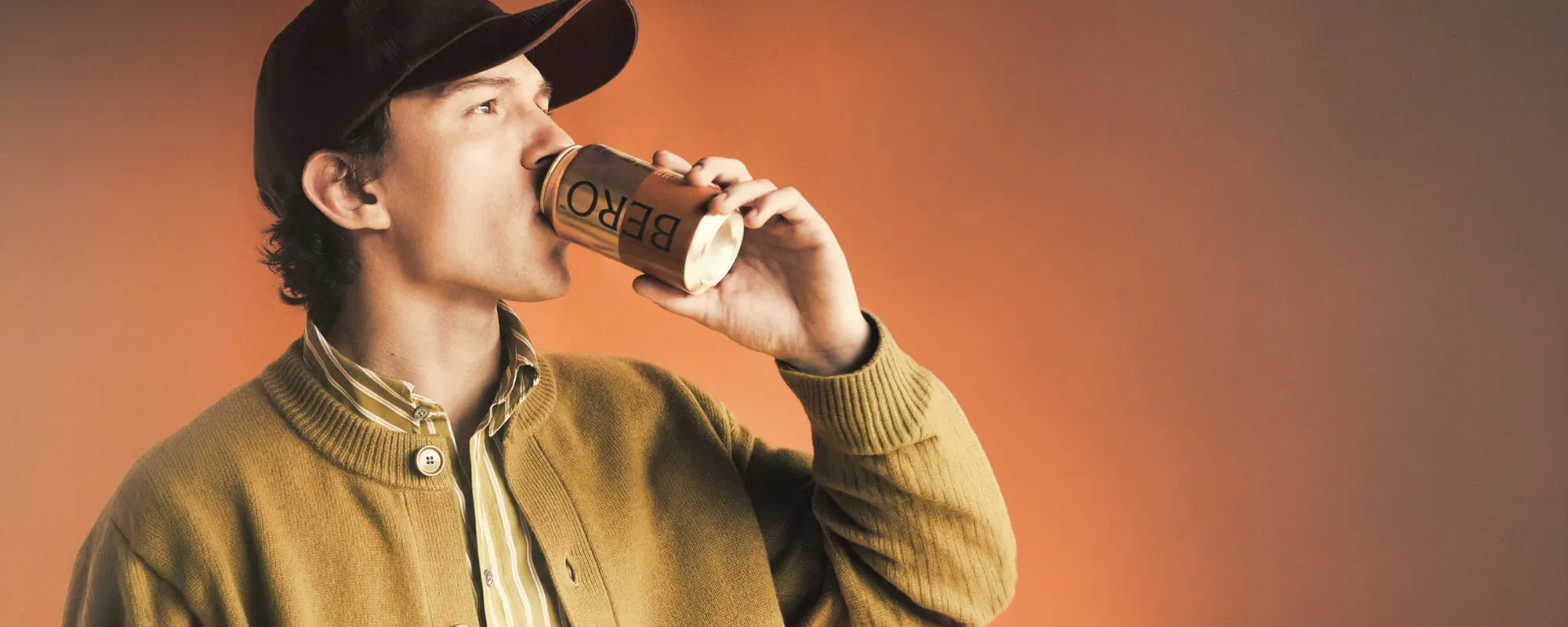 Man drinking a canned BERO non-alcoholic beer against an orange backdrop