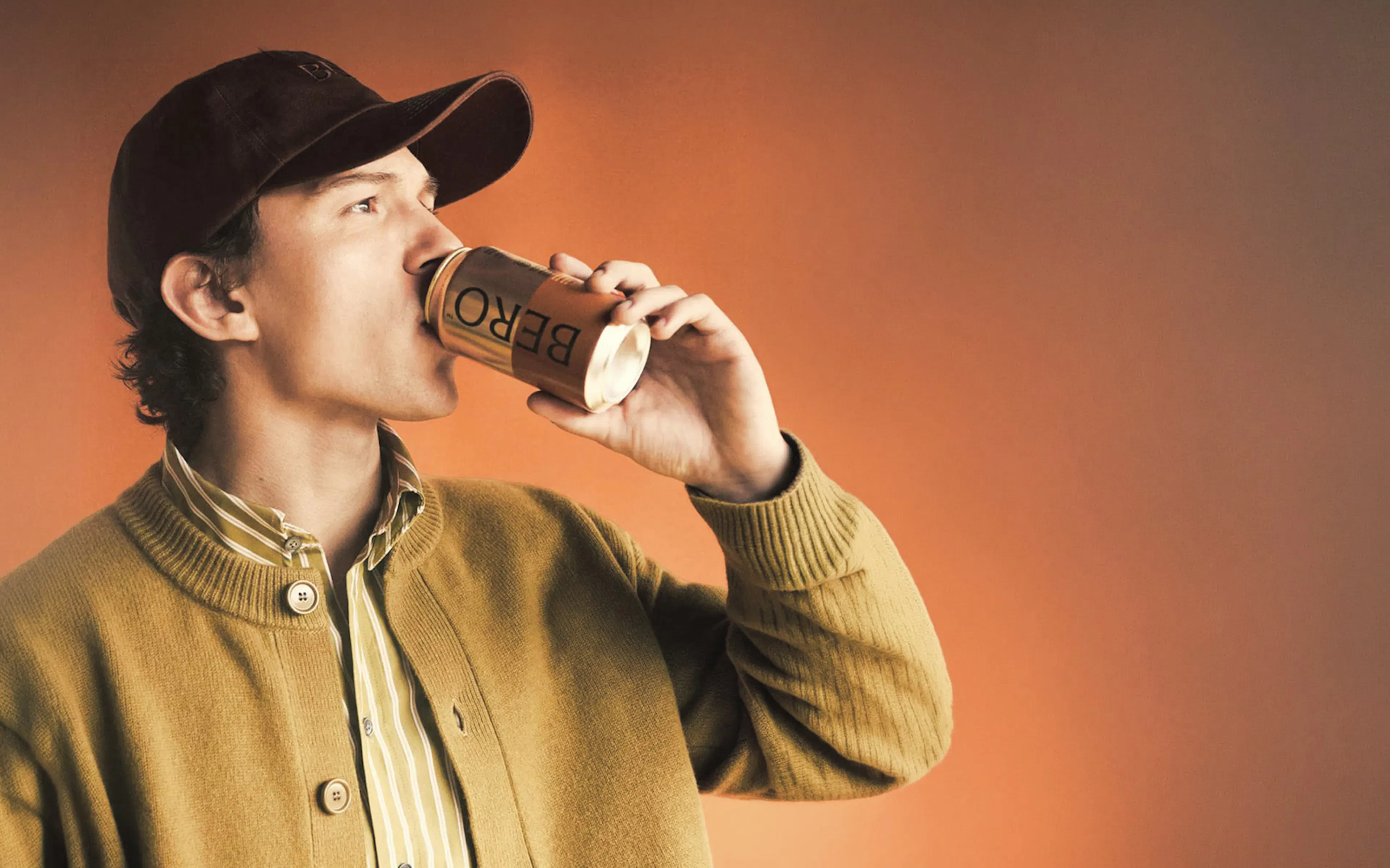 Man drinking a canned BERO non-alcoholic beer against an orange backdrop