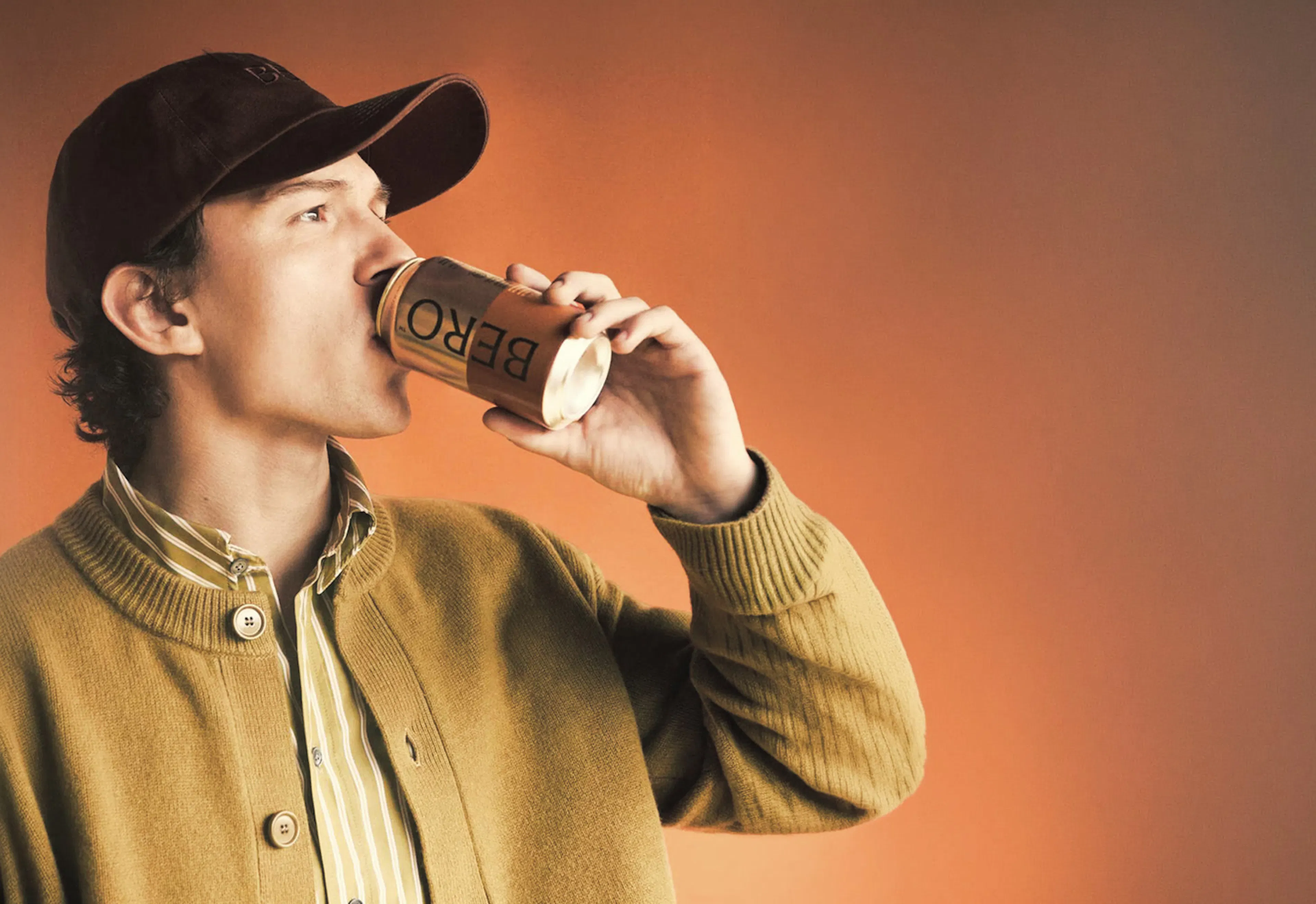 Man drinking a canned BERO non-alcoholic beer against an orange backdrop