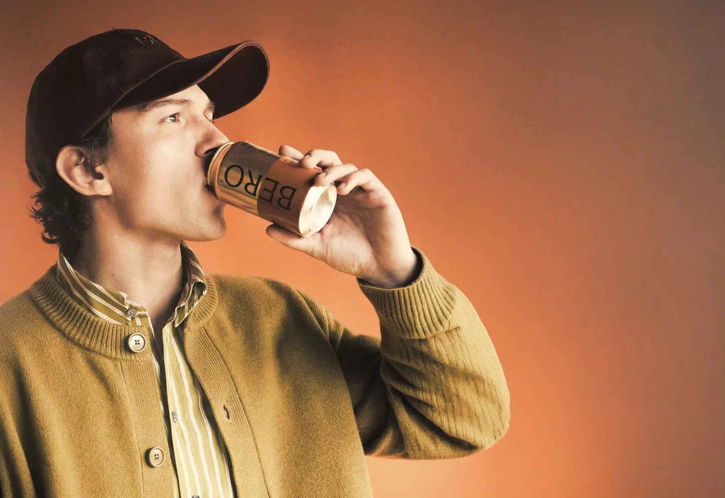 Man drinking a canned BERO non-alcoholic beer against an orange backdrop