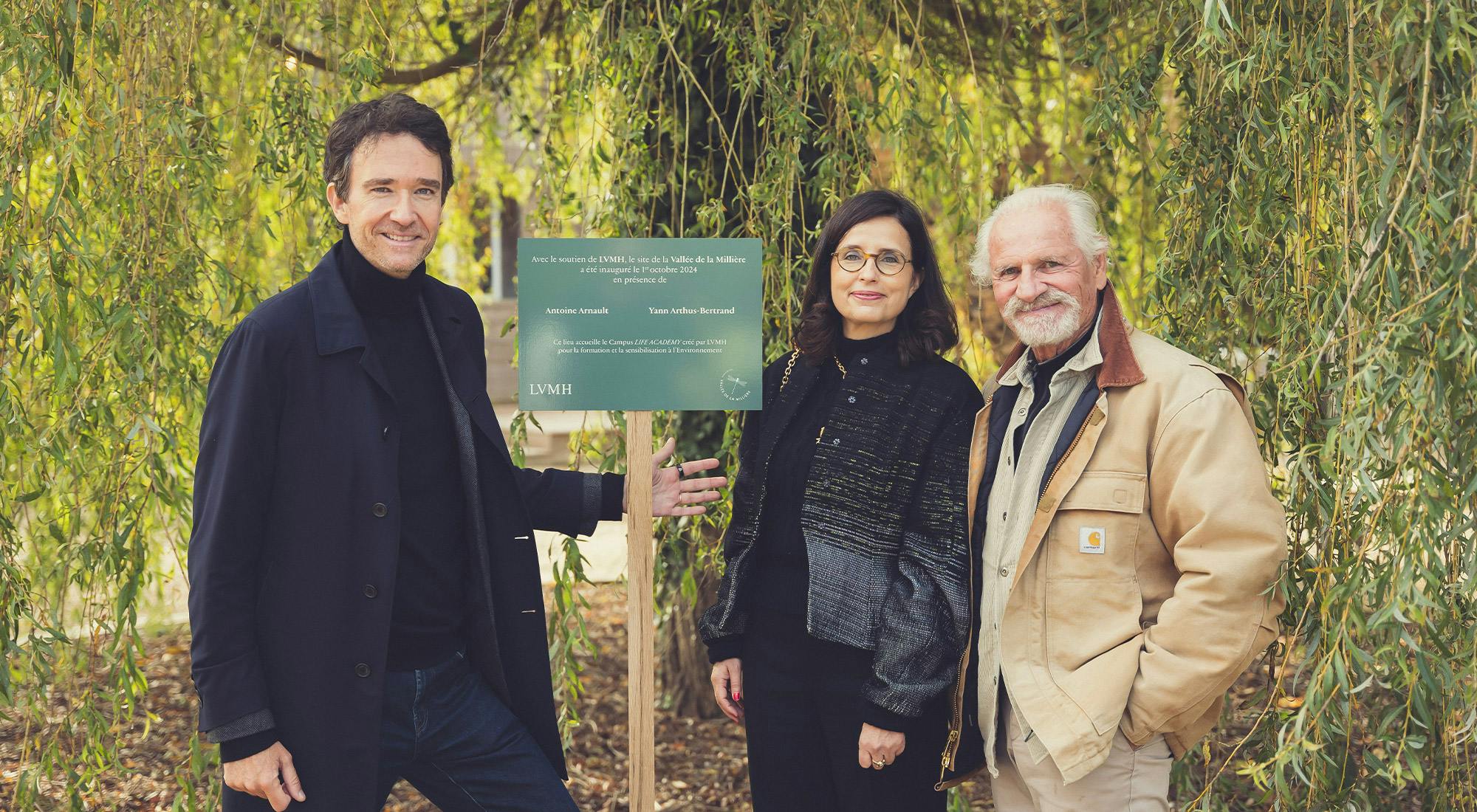 Hélène Valade, directrice développement & environnement et Antoine Arnaults membre du conseil d'administration du groupe LVMH posant avec Yann Arthus-Bertrand, président et fondateur de l'association de la Vallée de la Millière devant l'affichage rappelant la participation financière du groupe LVMH à la création du campus LIFE ACADEMY sur ce site.