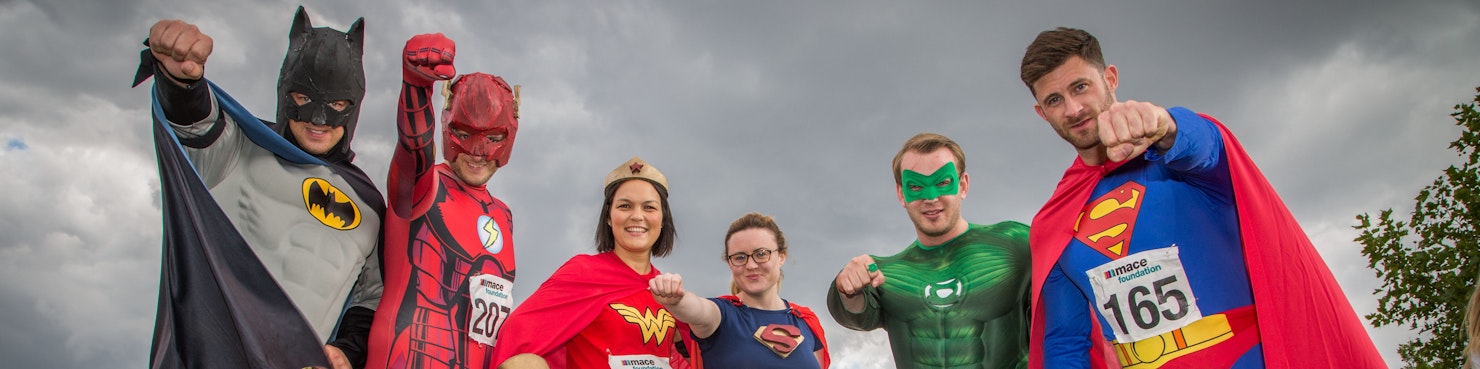 Group of people dressed as super heroes, smiling and punching their fists towards the camera