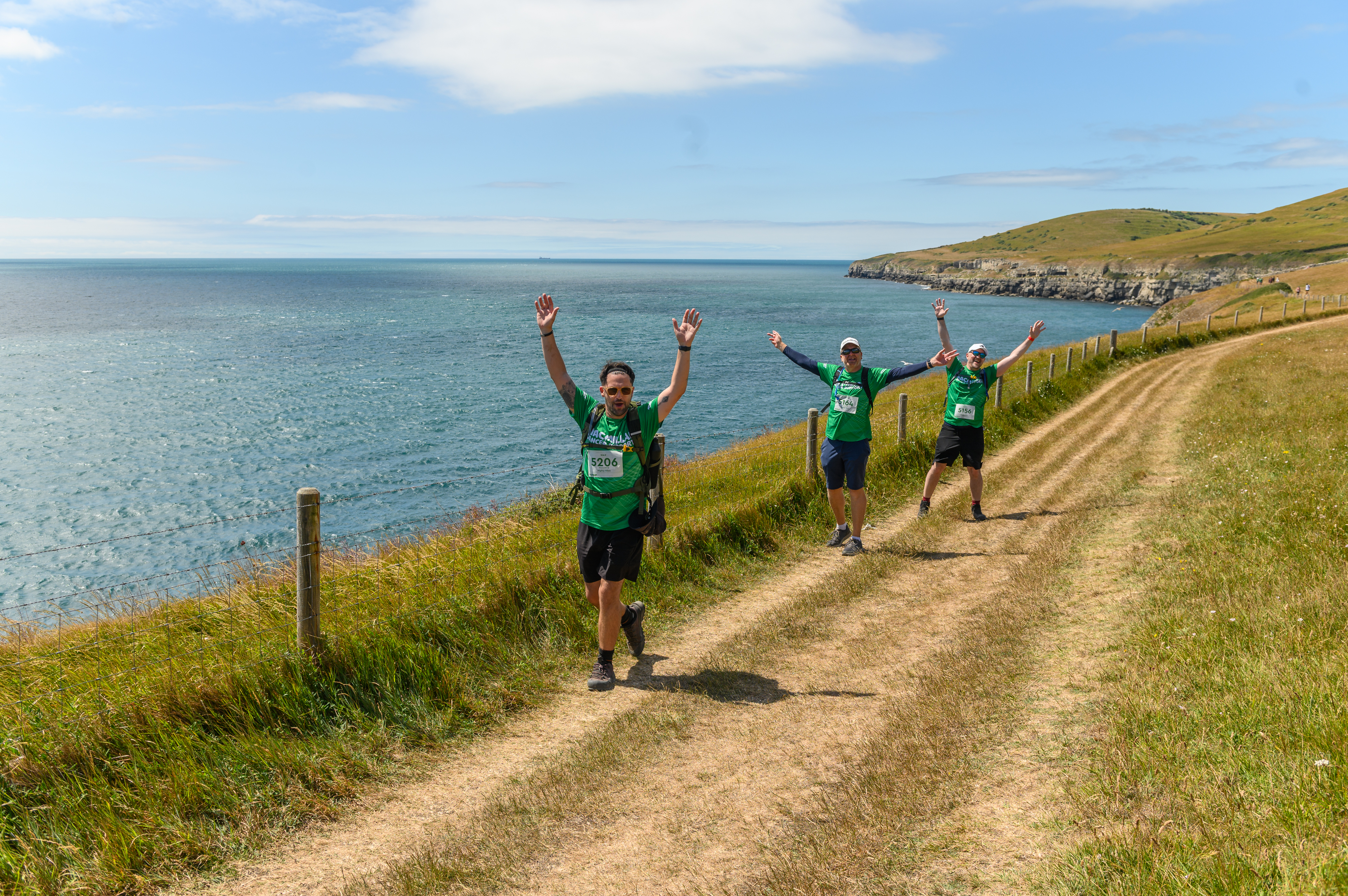 Three hikers walking along a coastal path waving at the camera.