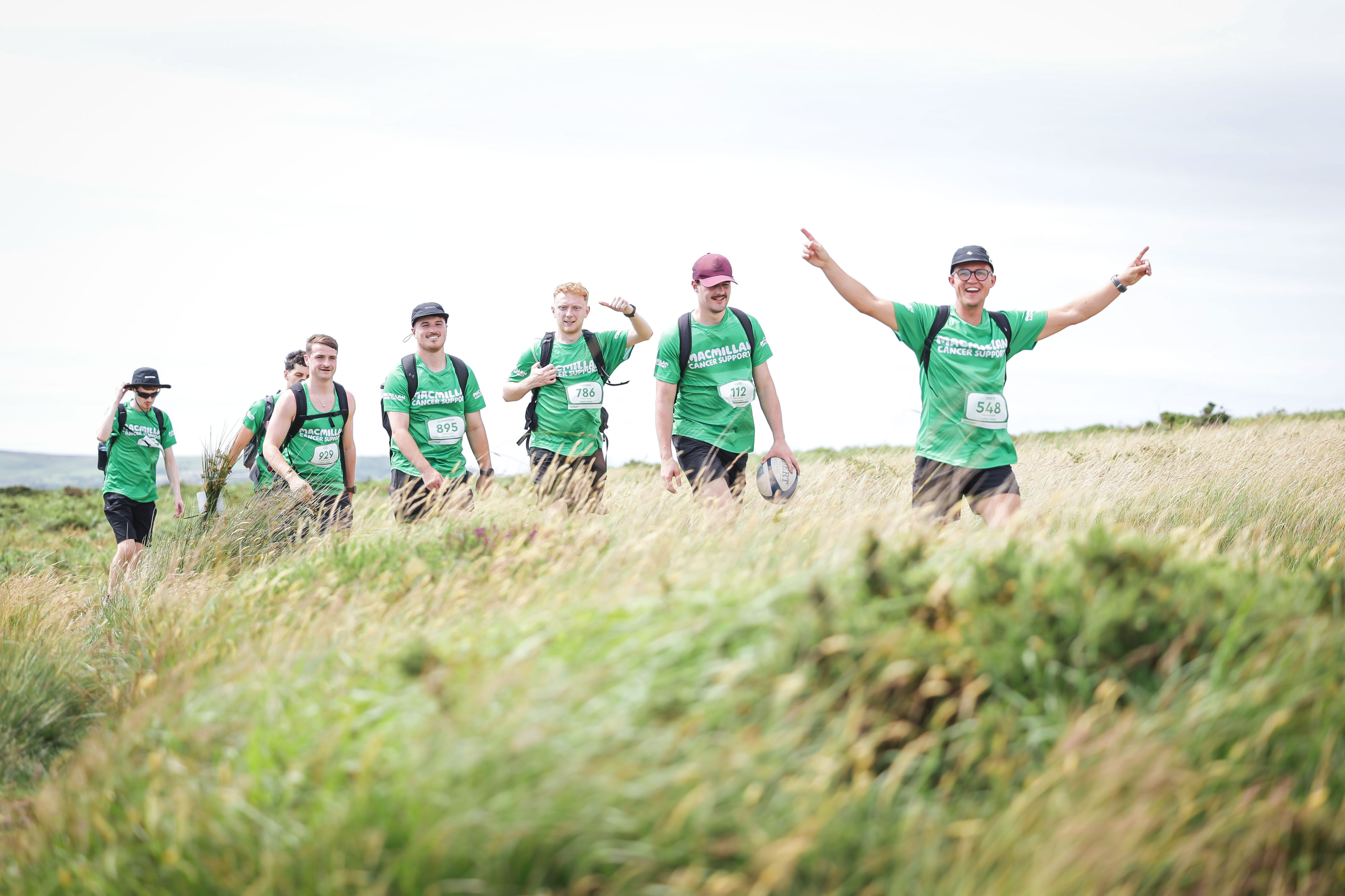 A smiling group of men hiking through long grass wearing Macmillan tops.