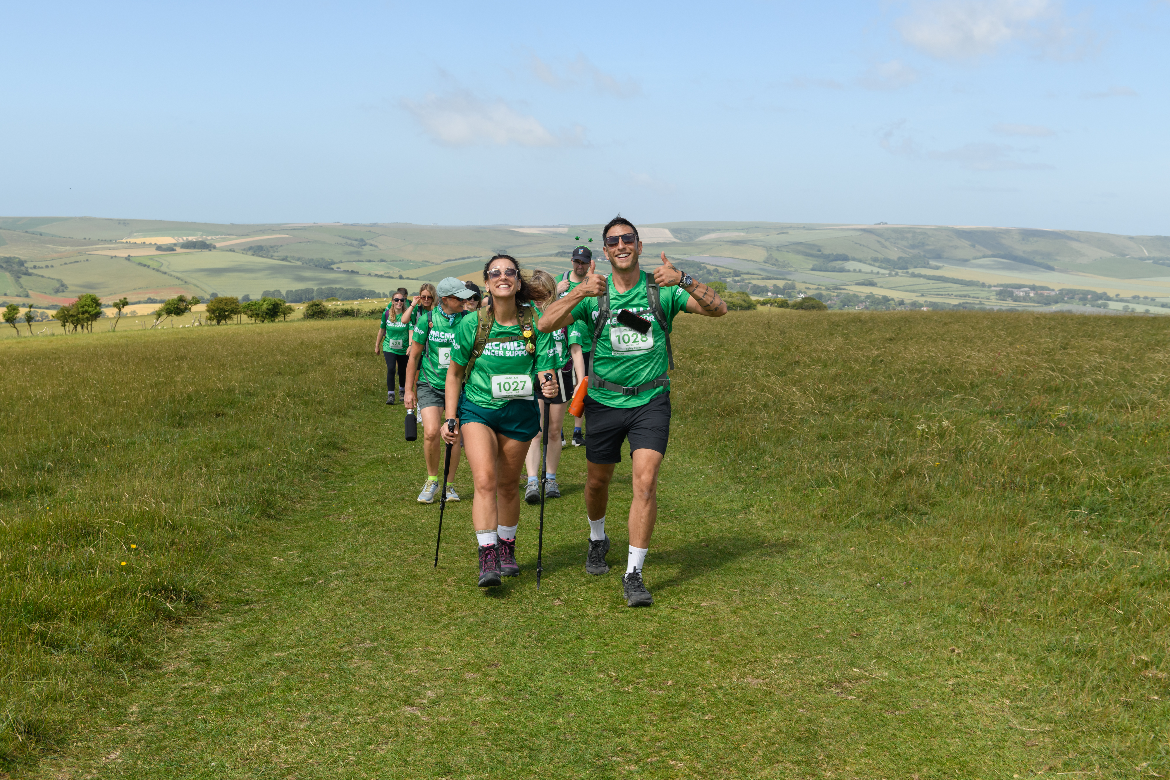 A group of Mighty Hikers walking along a grassy trail, visibly happy with smiles and thumbs up.