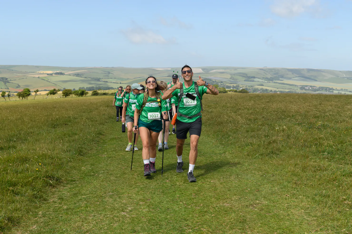 A group of Mighty Hikers walking along a grassy trail, visibly happy with smiles and thumbs up.