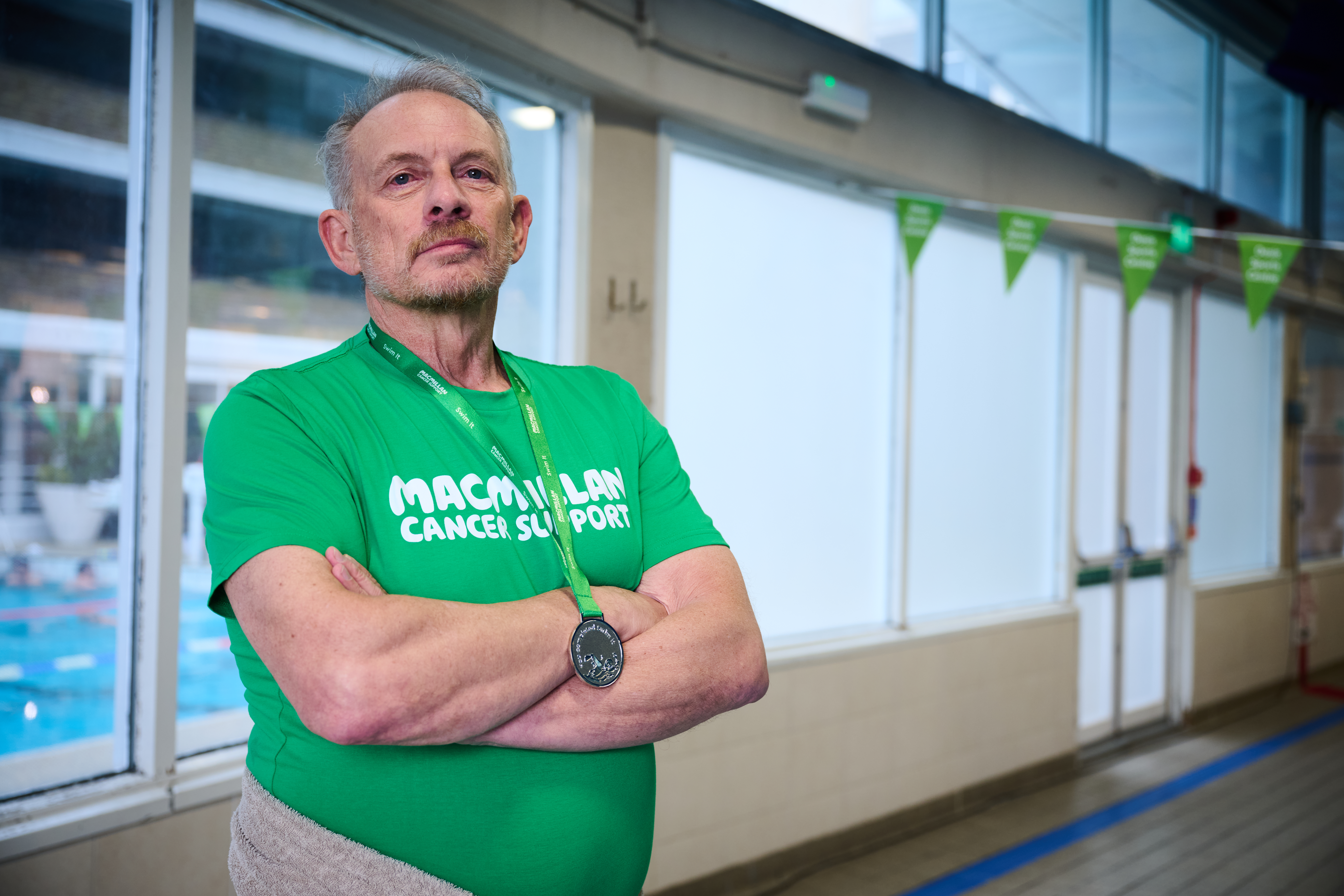 Nadio poolside, standing proudly with crossed arms in a Macmillan t-shirt with a medal round his neck.