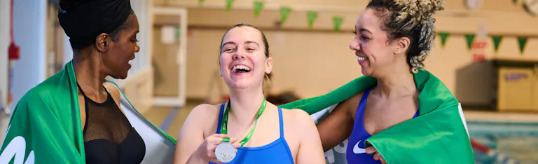 Three swimmers laughing with Macmillan towels and a medal.