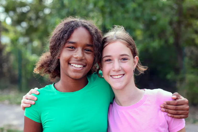 A black adolescent girl and white adolescent girl hugging.