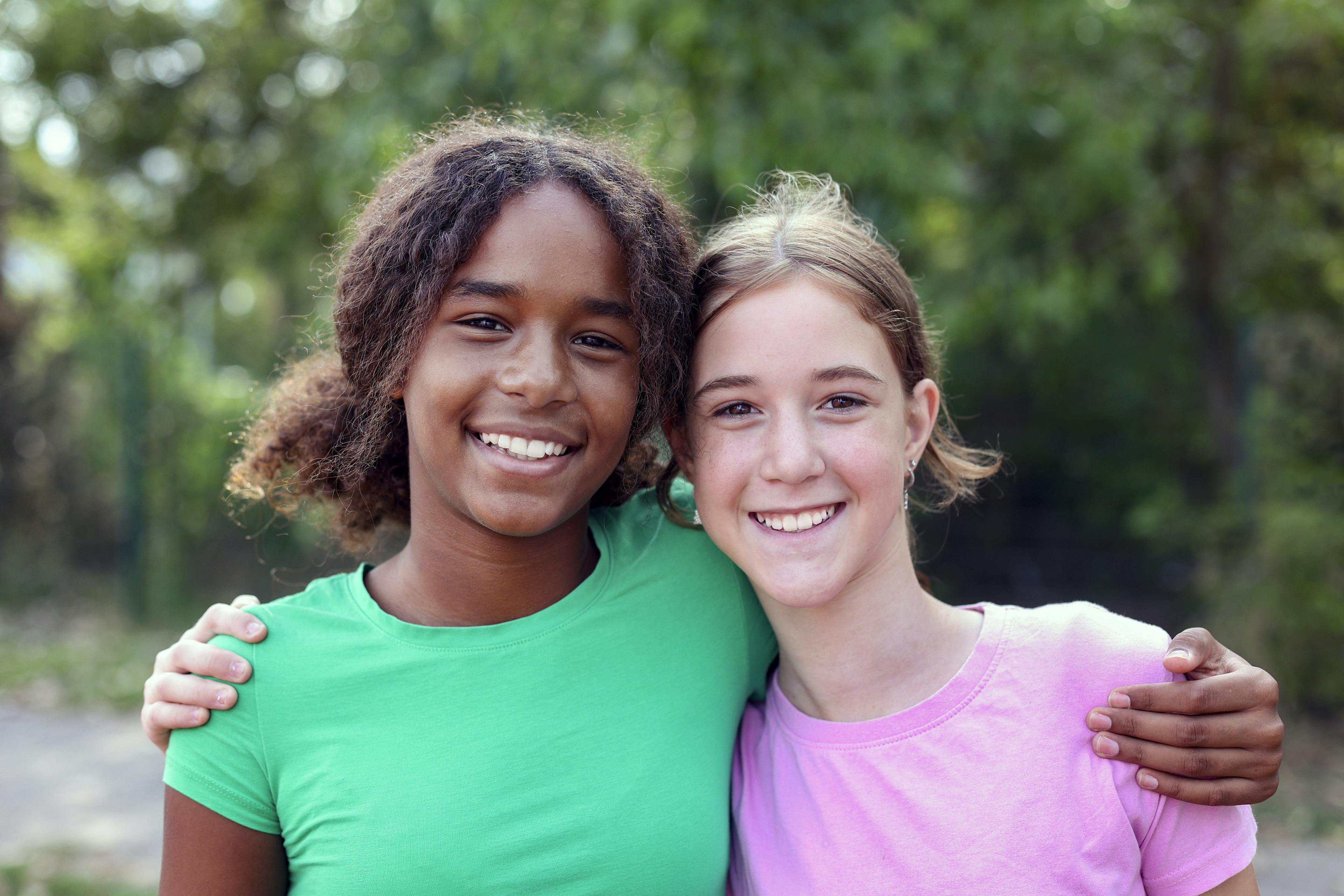 A black adolescent girl and white  adolescent girl hugging.