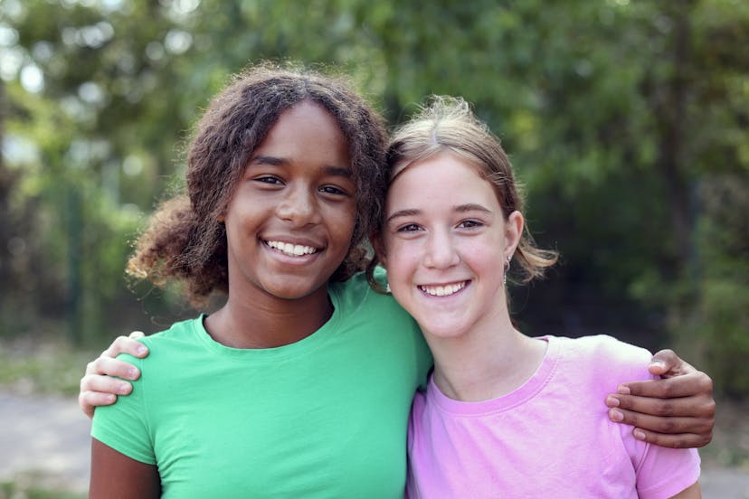 A black adolescent girl and white  adolescent girl hugging.